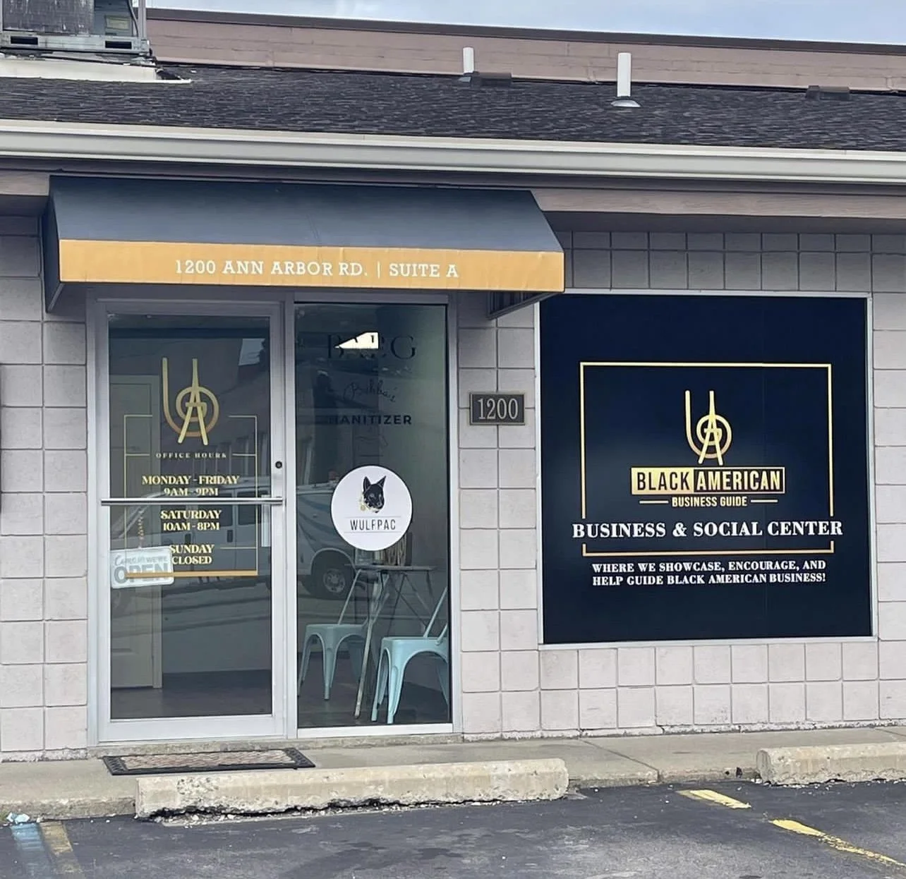 Front view of a building with signage for Black American Business Guide and Social Center, with hours of operation listed on the door, and a logo of a black dog with the text "WULFPAC" on the door window.