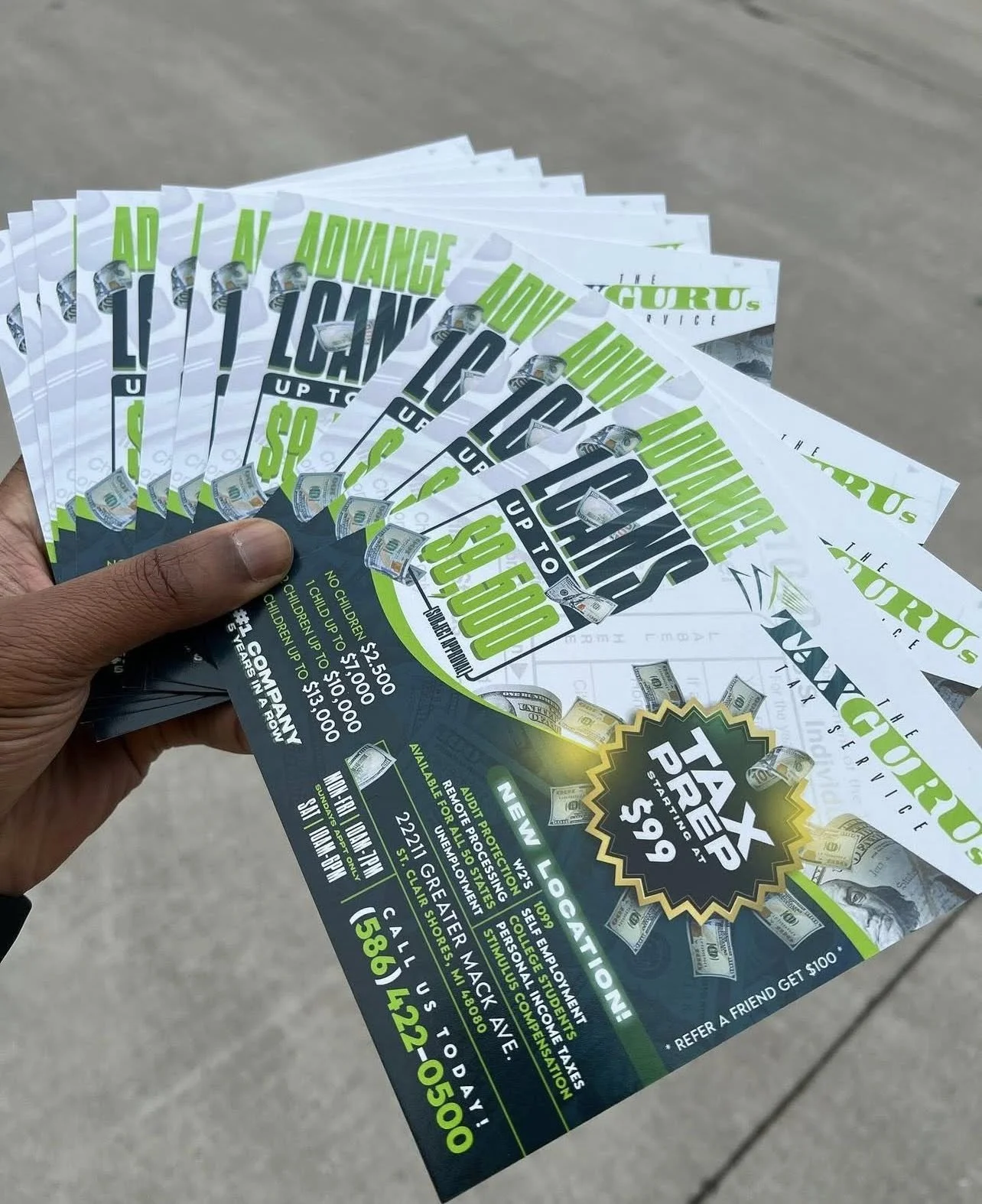 A person holding multiple flyers advertising a tattoo studio promotion for $99, with a background showing a concrete sidewalk.