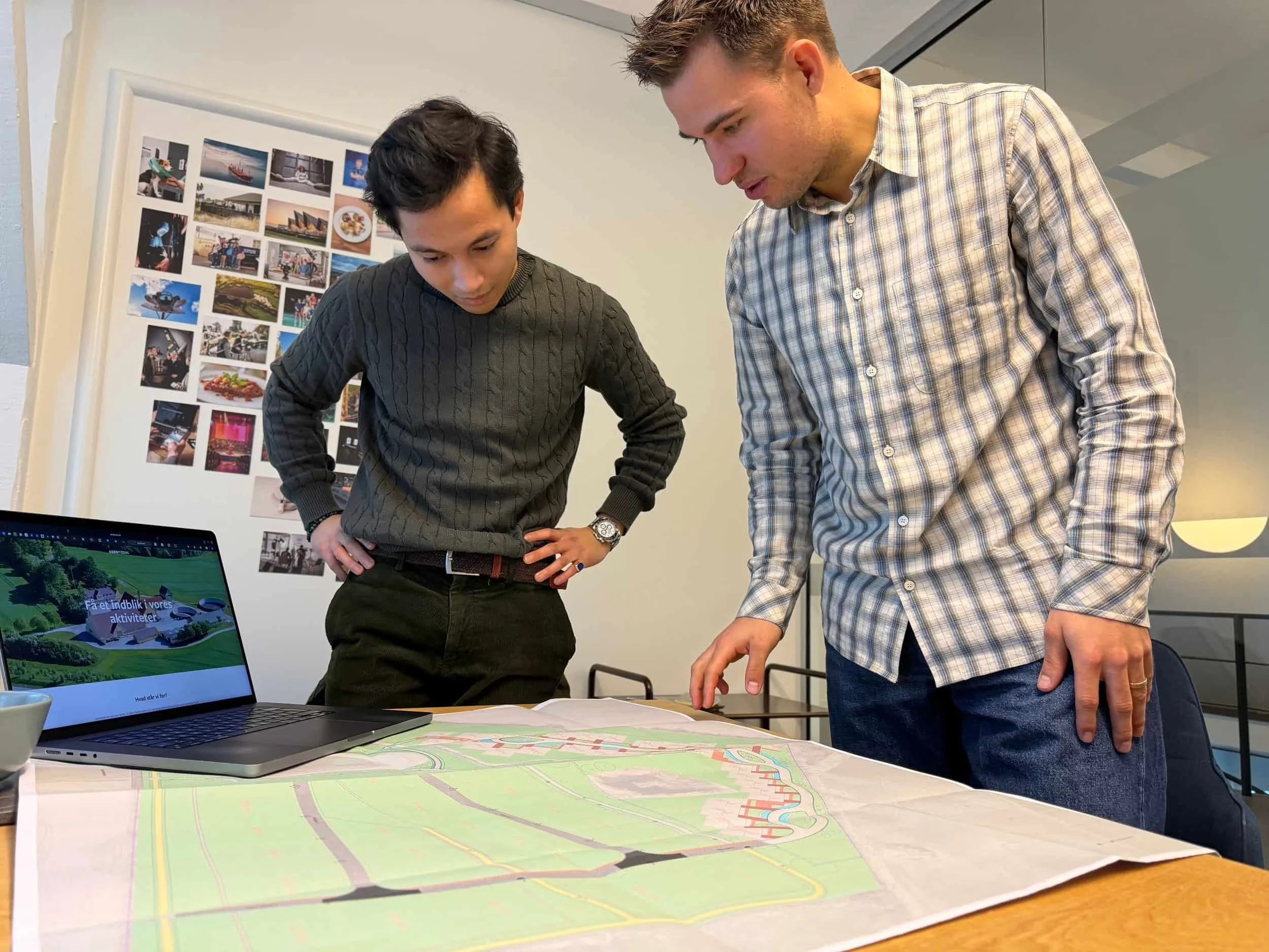 Nikolaj fra R.E. Ejendomme og Emil fra ELS Production står og ser på et stort matrikelkort på et bord i et mødelokale.