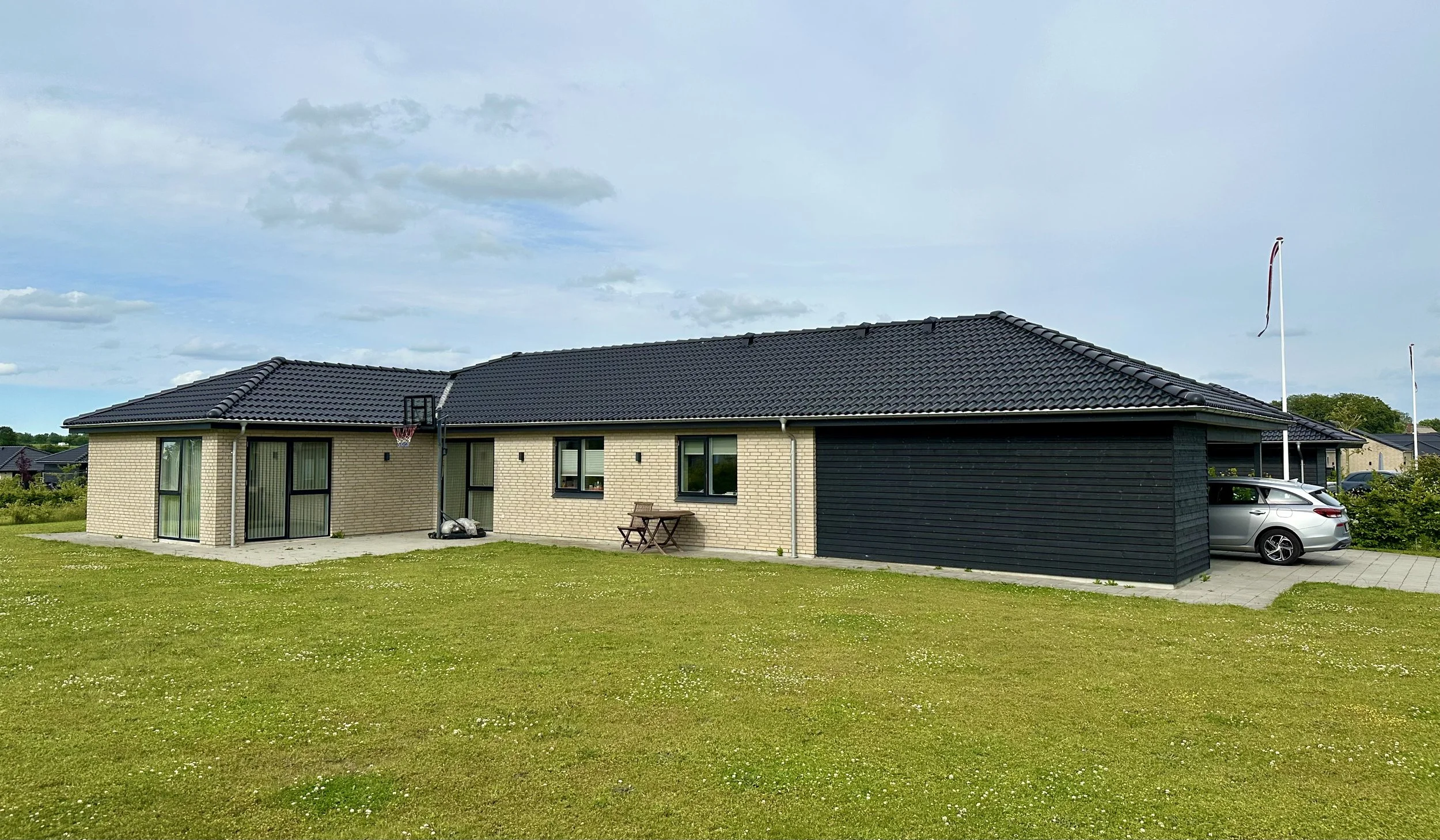 Et moderne, enkelt hus i Ringe med et sort tagstenstag, lyse murstensvægge og en garage med en bil parkeret.