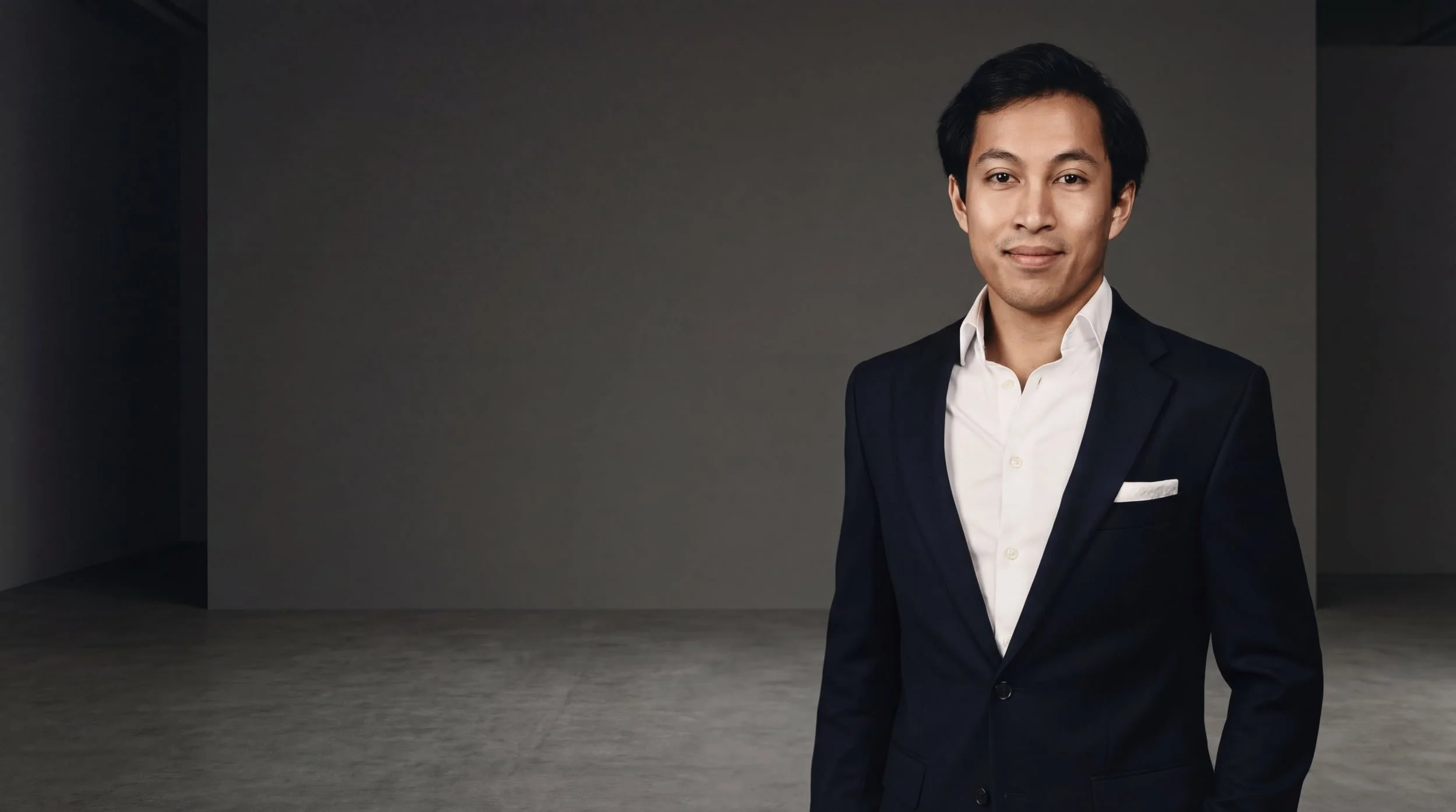 Nikolaj fra R.E. Ejendomme står i et sort jakkesæt og hvid skjorte foran en grå baggrund.