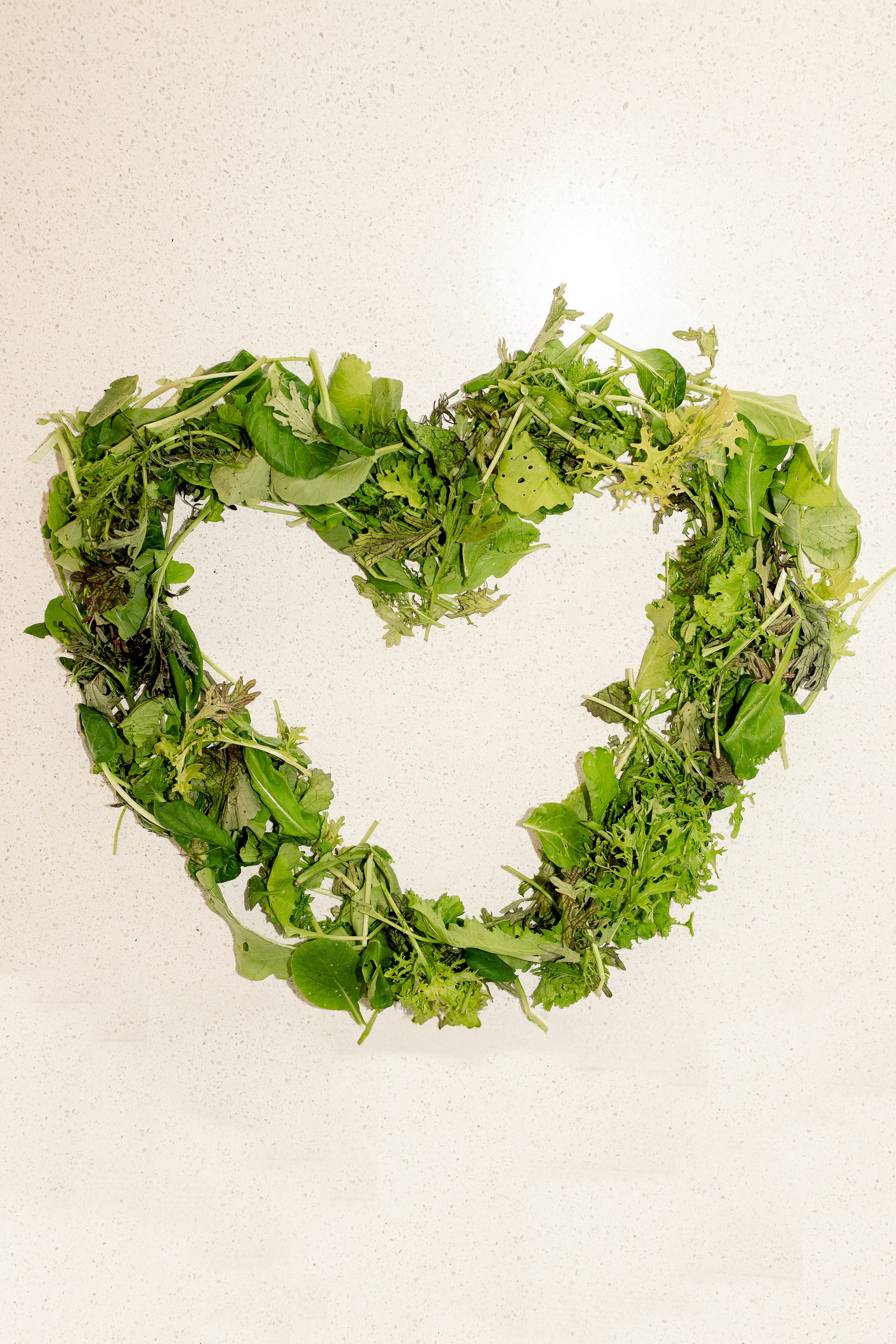 Heart shape made of various green leafy vegetables on a plain background.