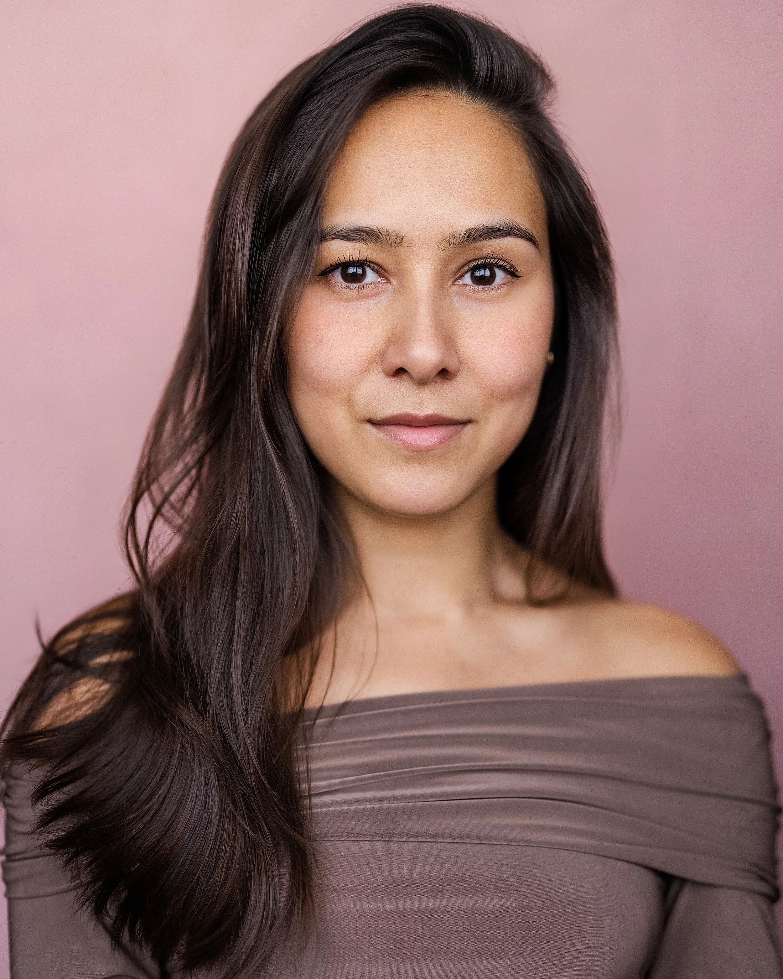 Actor Marielle Young, wearing an off-shoulder taupe top, standing against a pink background.