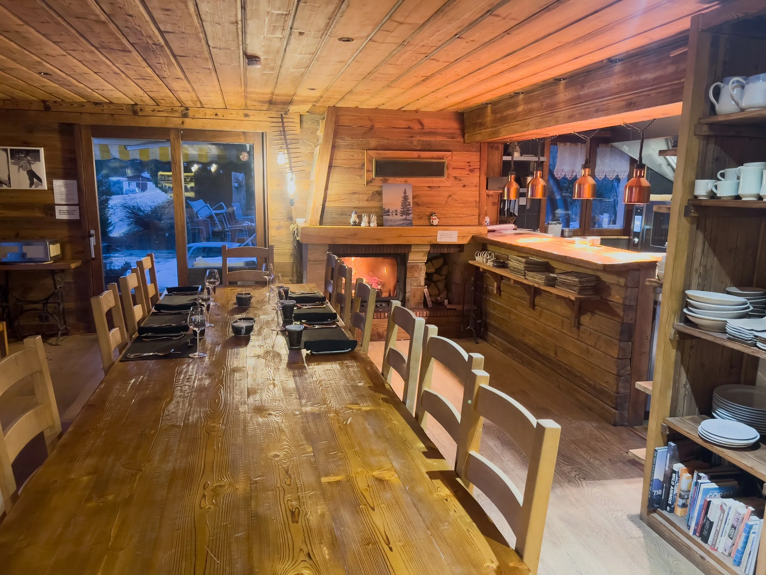 Luxury chalet dining area at Chalet Sandy in Les Gets with long wooden table, open-plan kitchen, and mountain views in the French Alps.