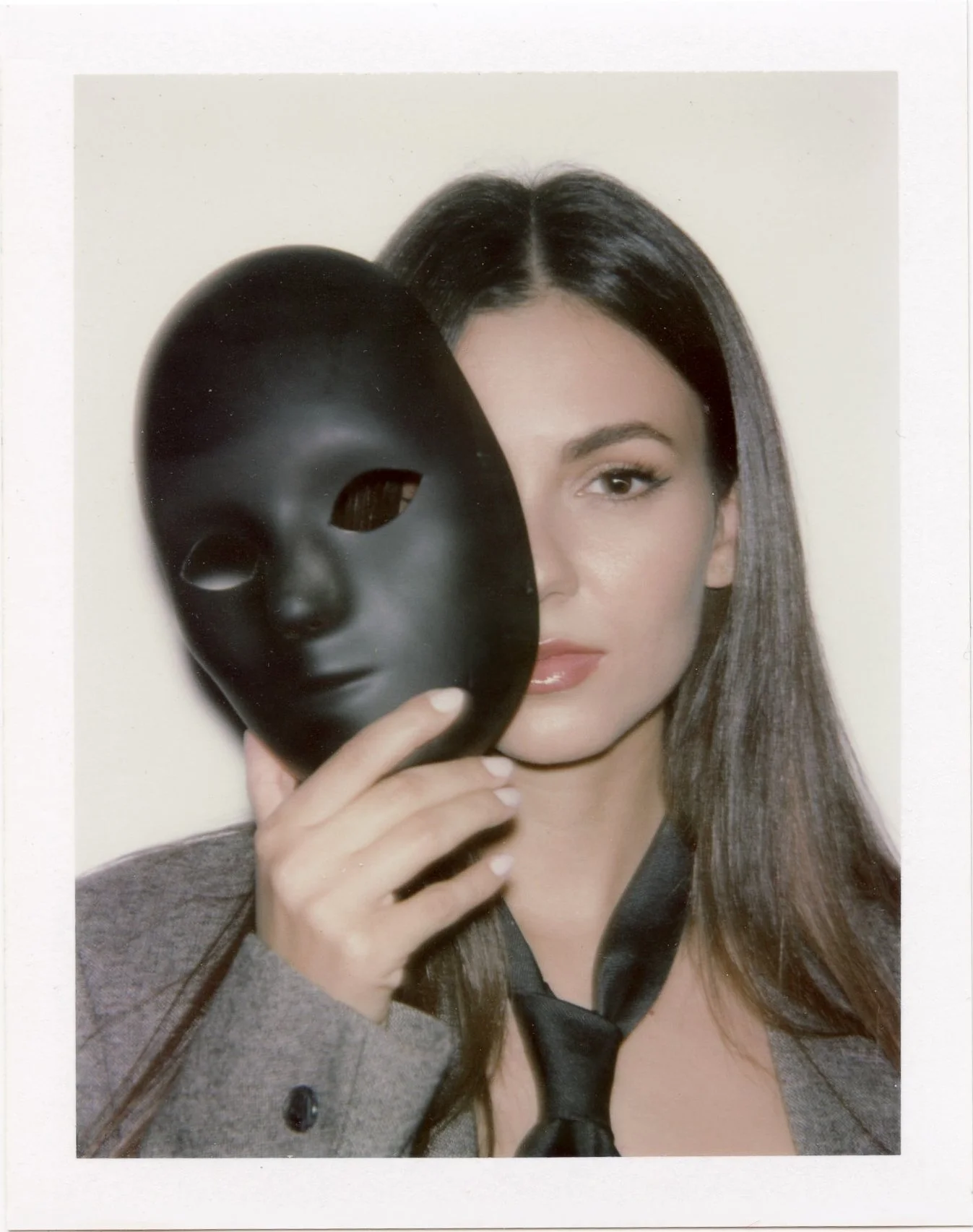 Woman with long dark hair holding a black mask with eye holes in front of her face. Vitcoria Justice, polaroid, Victoria Justice by Dan Pop