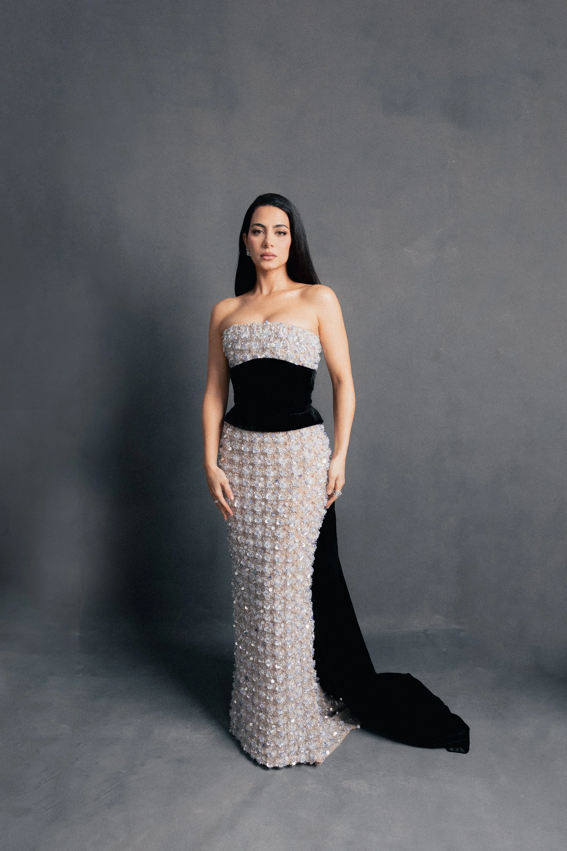 Actress Emeraude Toubia posing in a full-length strapless silver sequin gown with a black velvet waist corset and train for a Vogue Mexico editorial.