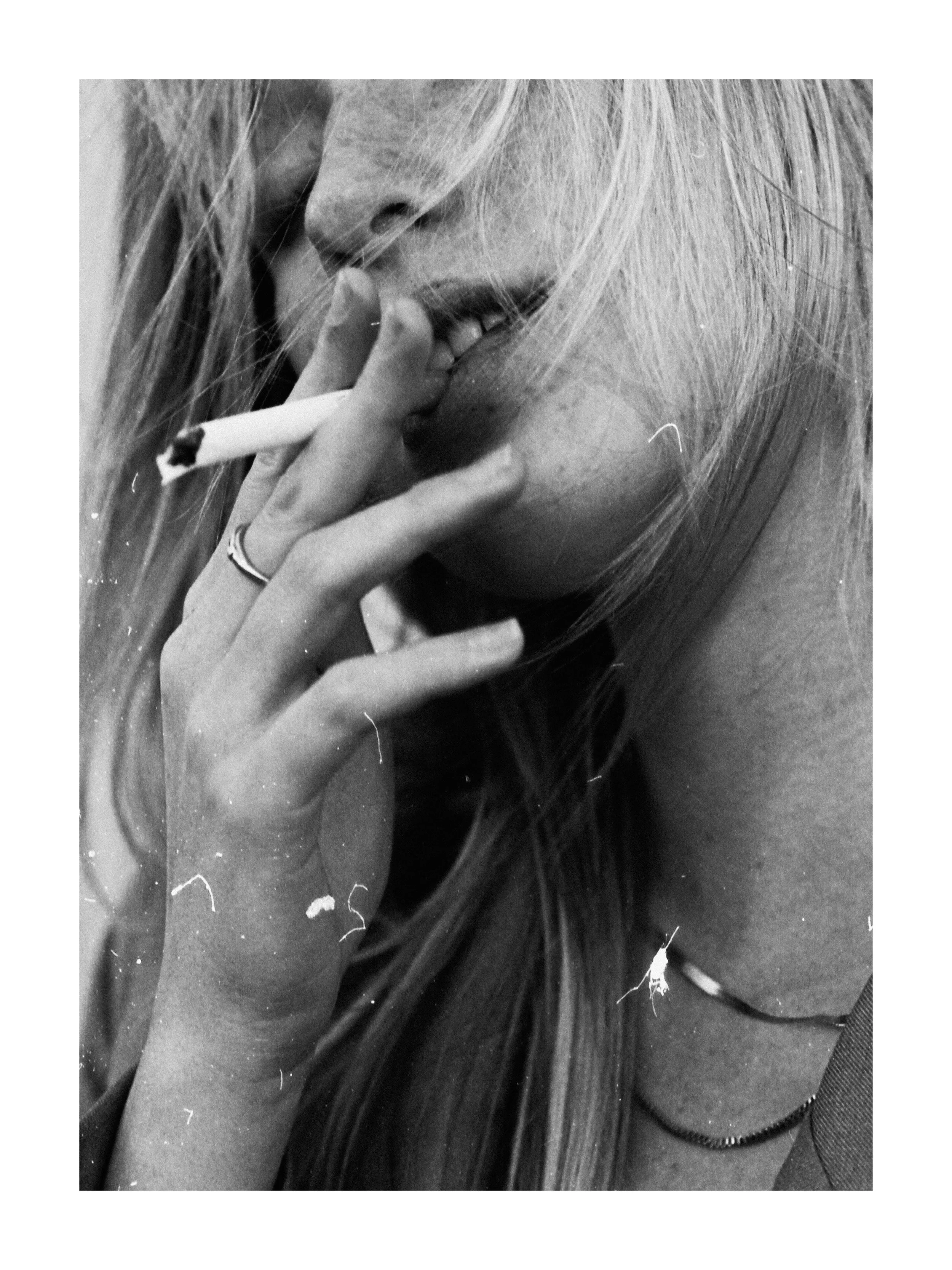 Close-up of a person with long hair, holding a cigarette near their mouth, with some hair partially covering their face.