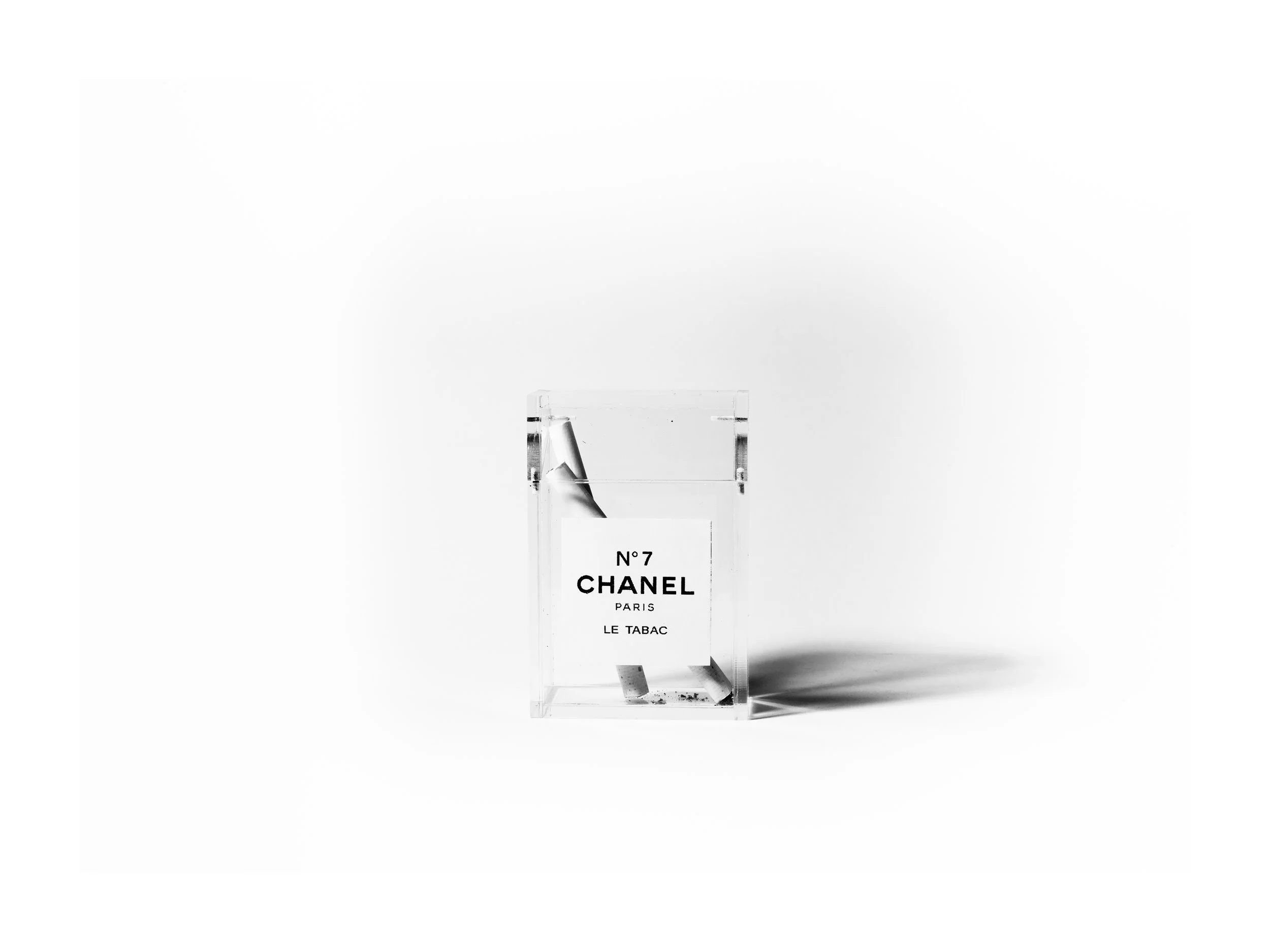 A black and white photograph of a Chanel N°7 perfume bottle against a white background, with a shadow cast to the right.