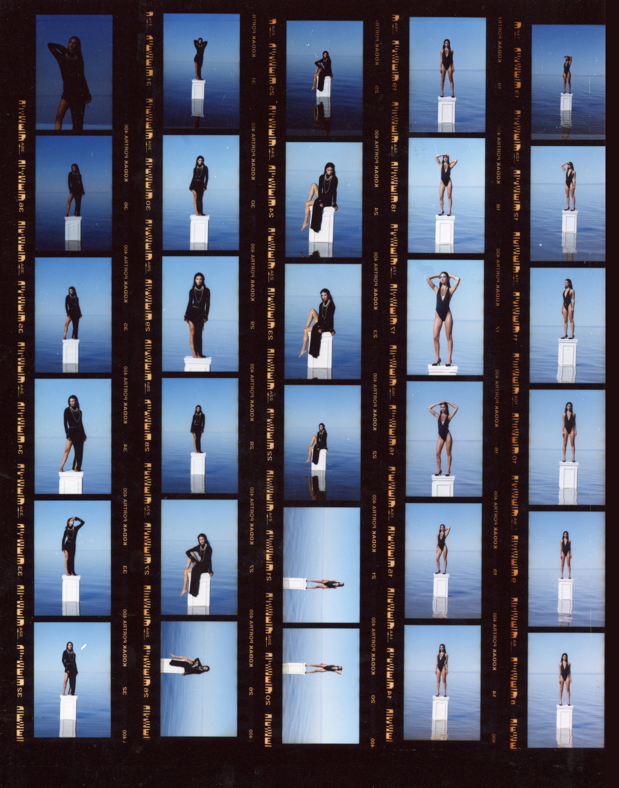 A strip of 24 photo negatives showing a woman in various poses on a white pedestal against a blue sky and water background, with some images of her lying or sitting on the pedestal.