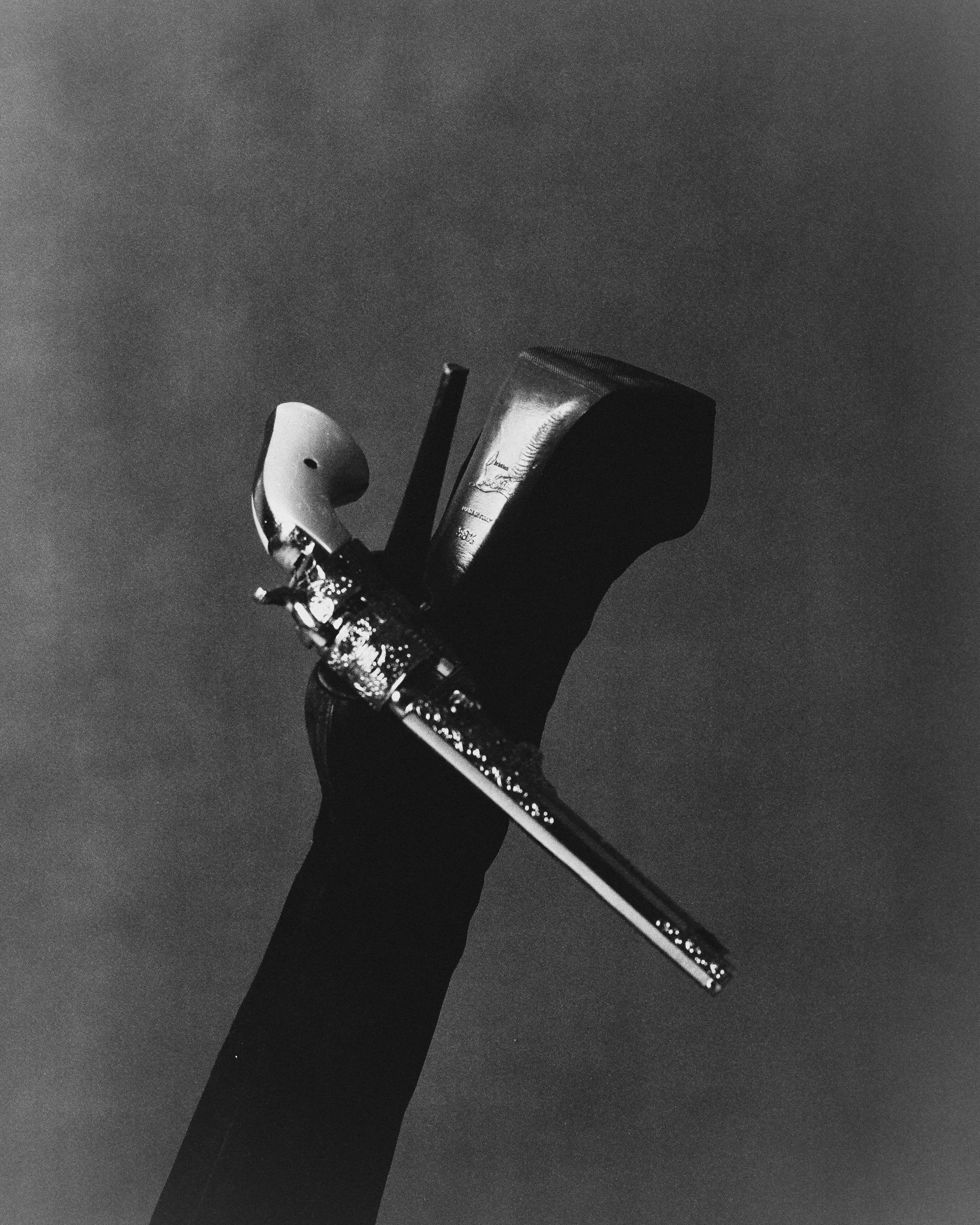 Hand holding a golf club, a golf ball, and a golf tee in black and white.