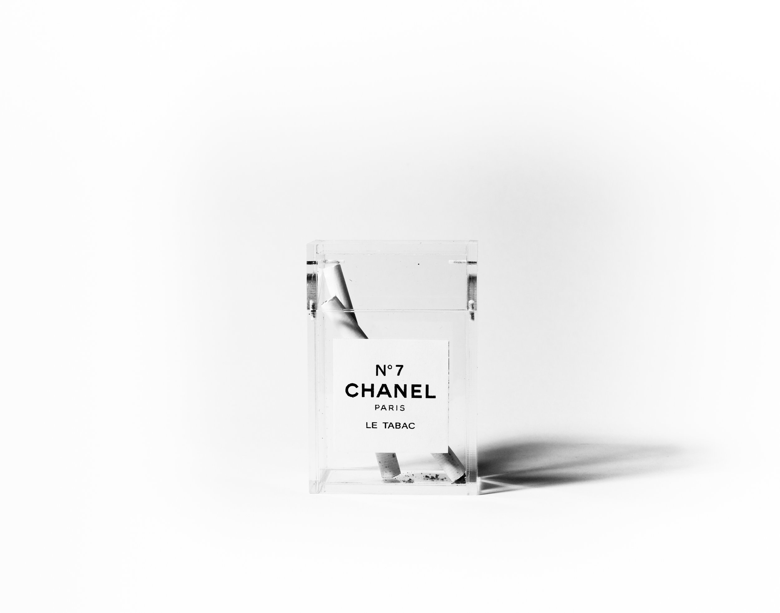 A transparent Chanel N°7 perfume bottle with a perfume rollerball resting on a plain white background.