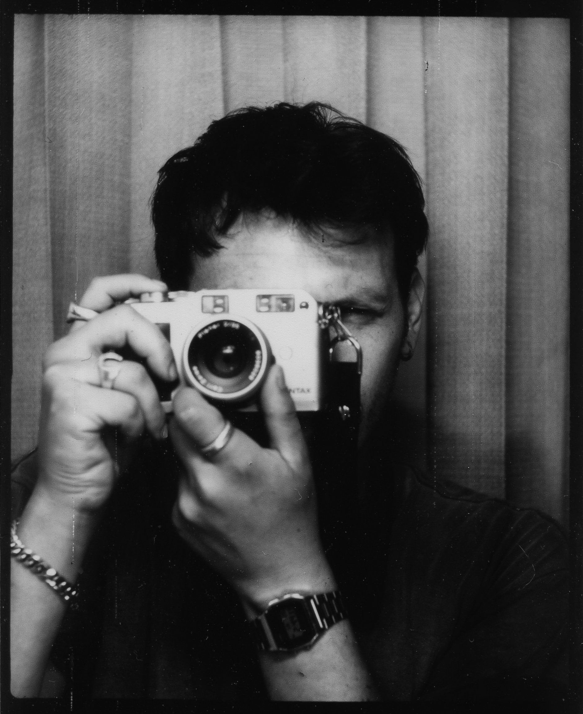 Person taking a photo in front of a mirror with a camera, with a curtain background.