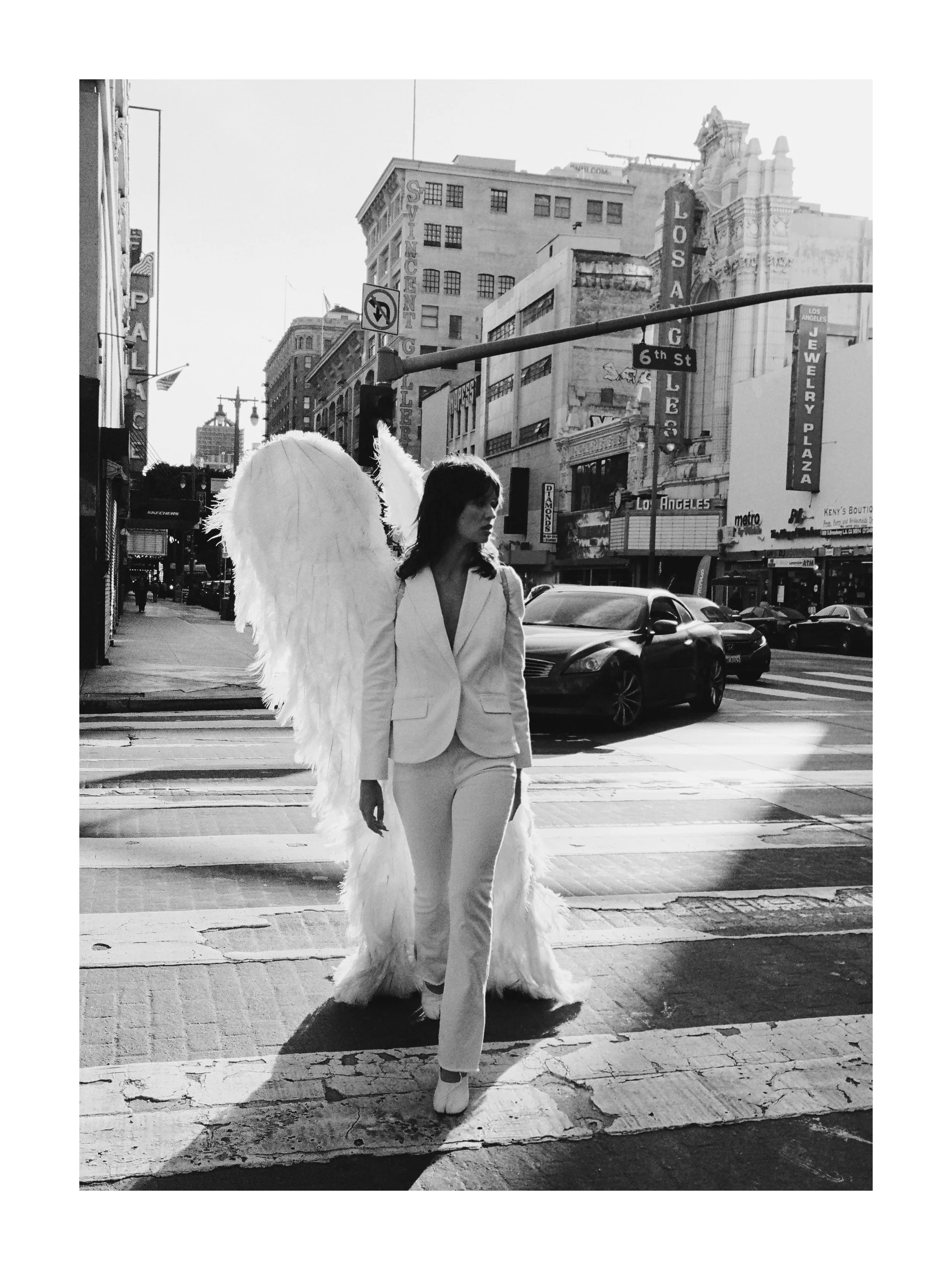 Woman with angel wings walking across a city crosswalk in black and white.