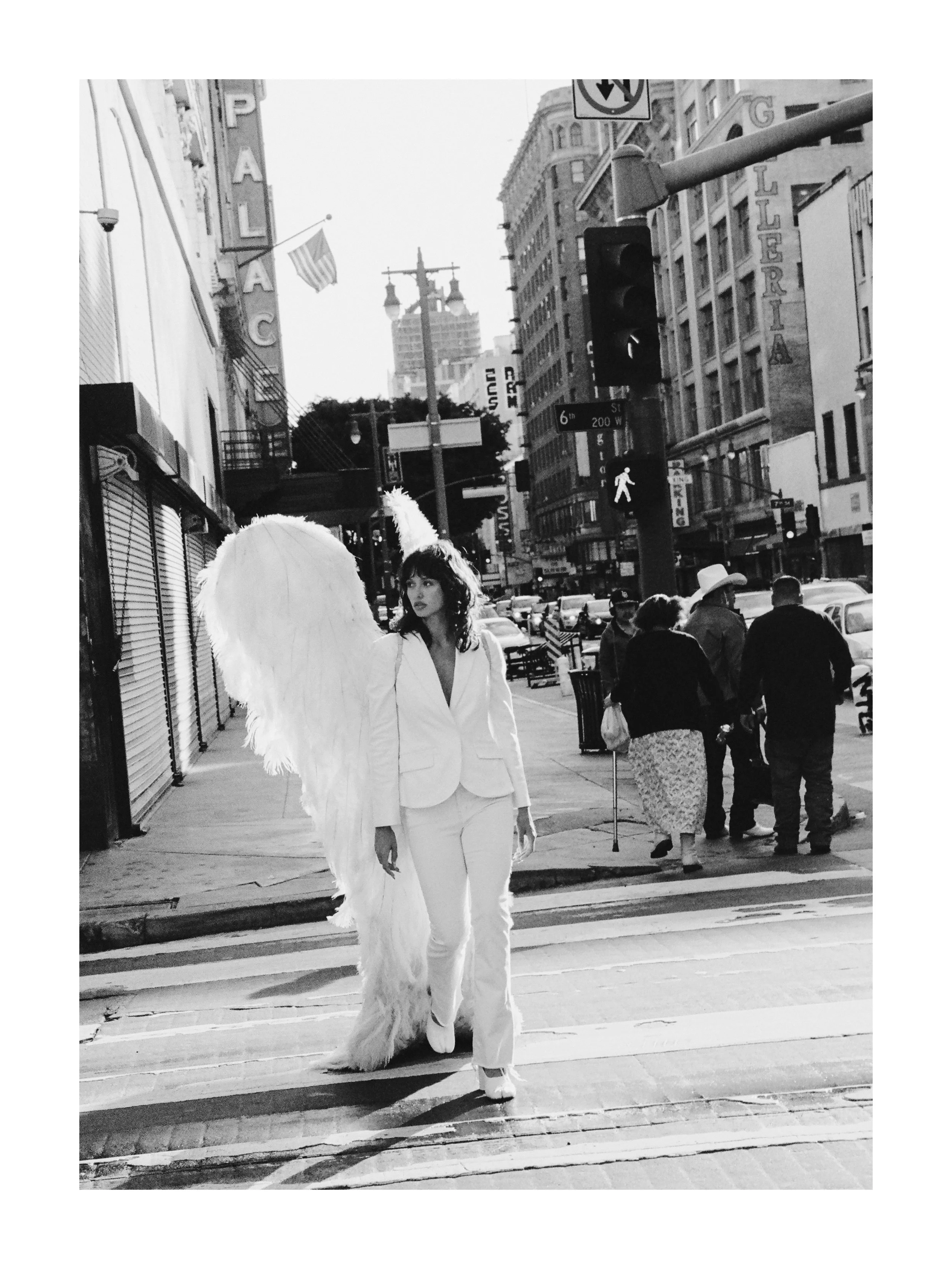 A woman in a white suit with angel wings walking across a city street in black and white.