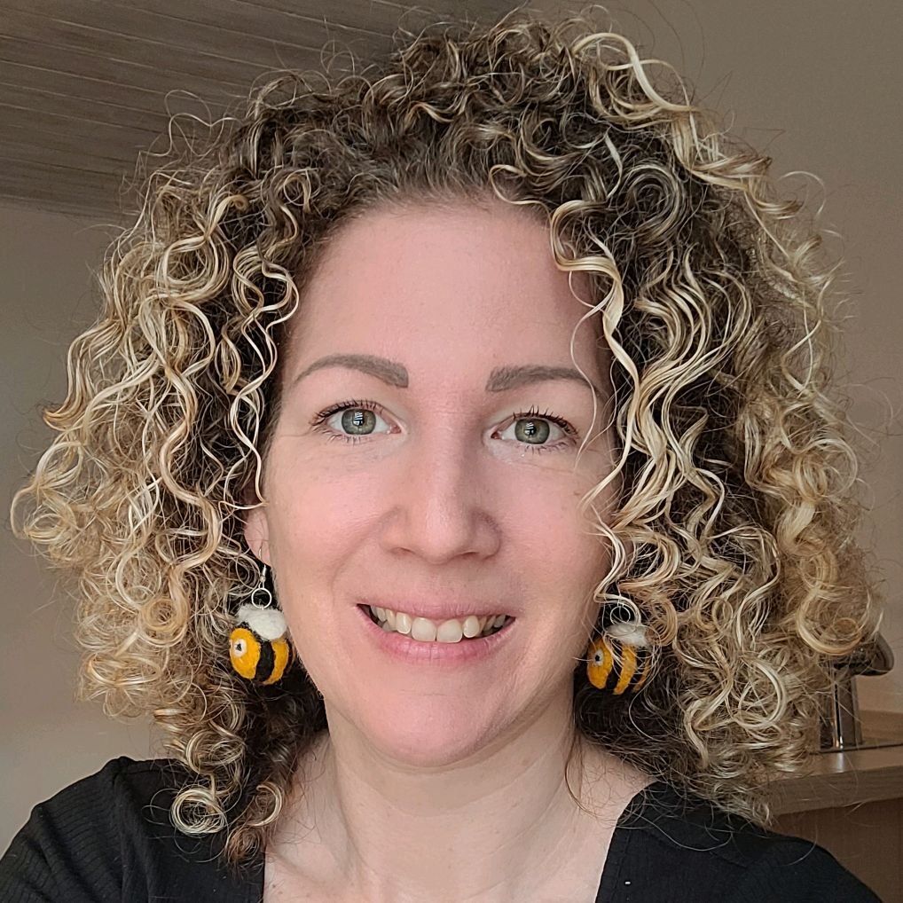 Nahaufnahme eines lachenden Mädchens mit lockigem Haar und Bienen-Ohrringen.
