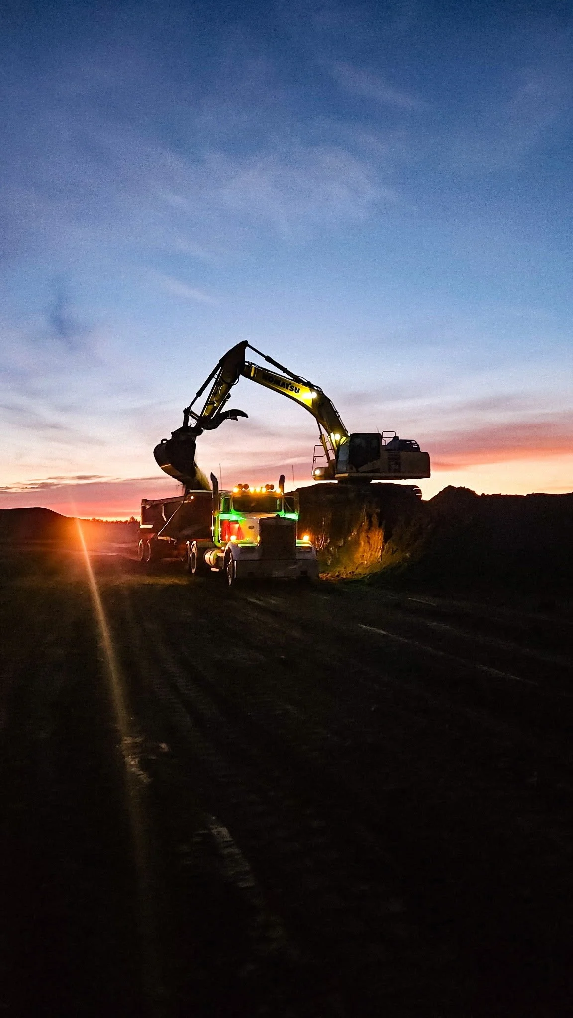 Farmer working at sunset using a large excavator and dump truck on farmland.