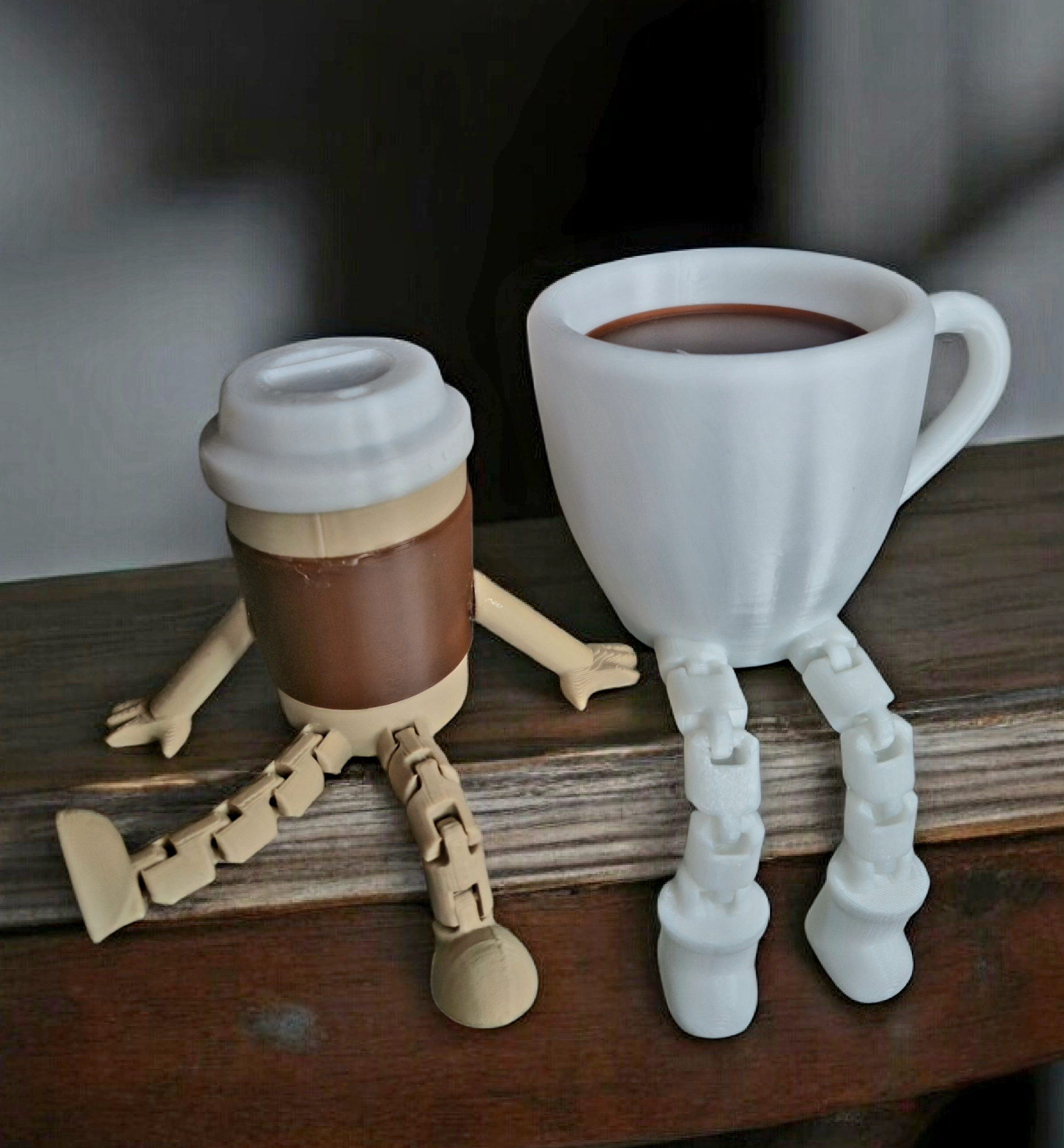 Zwei Tassen mit Kaffeetassen und Kunststoffbeinen, die wie kleine Kreaturen aussehen, stehen auf einem Holztisch.