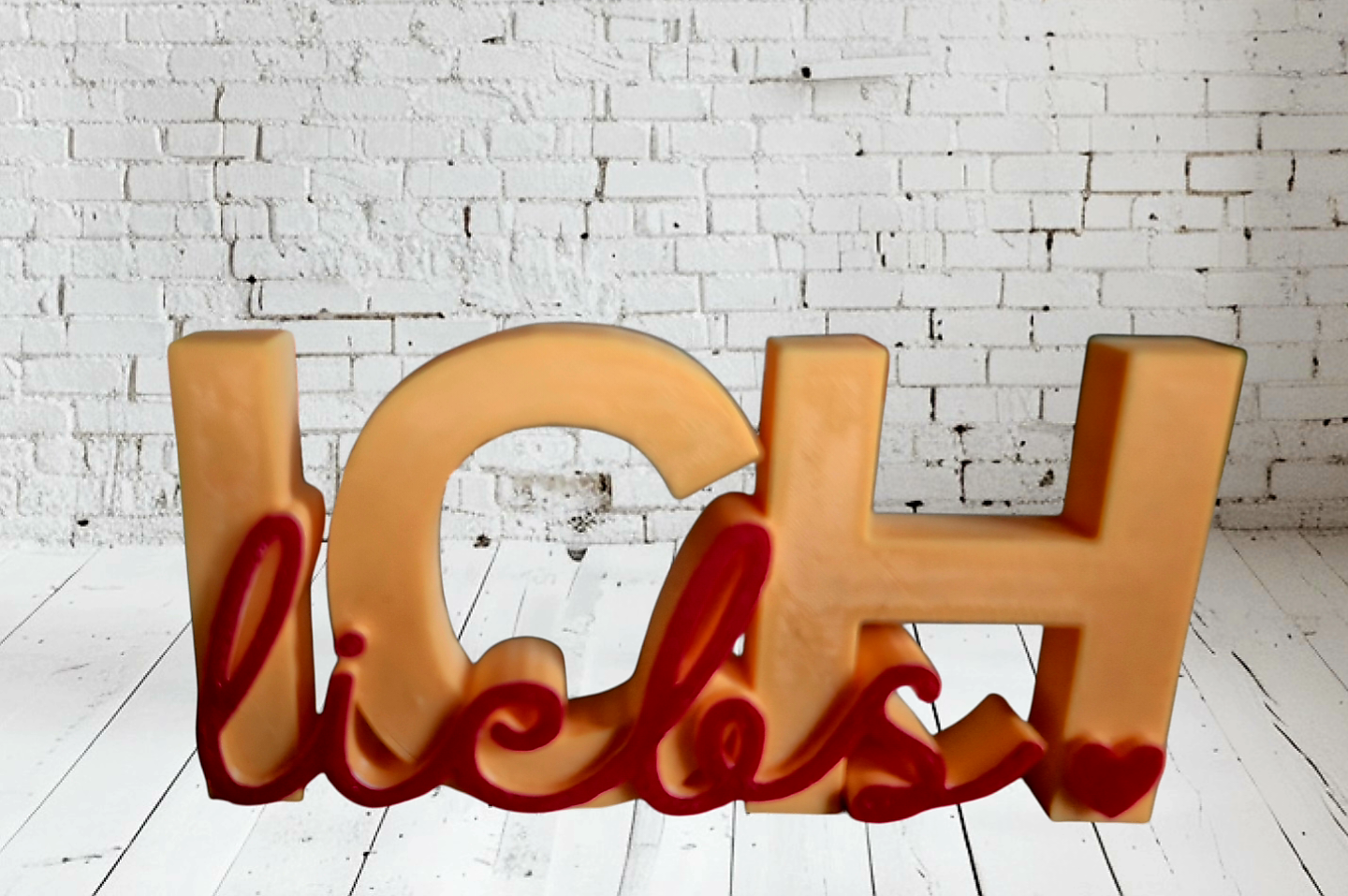Kunststoffbuchstaben, die das Wort "Ich" bilden, mit roten und pinken dekorativen Elementen an der Unterseite, vor einer weißen Ziegelwand. 