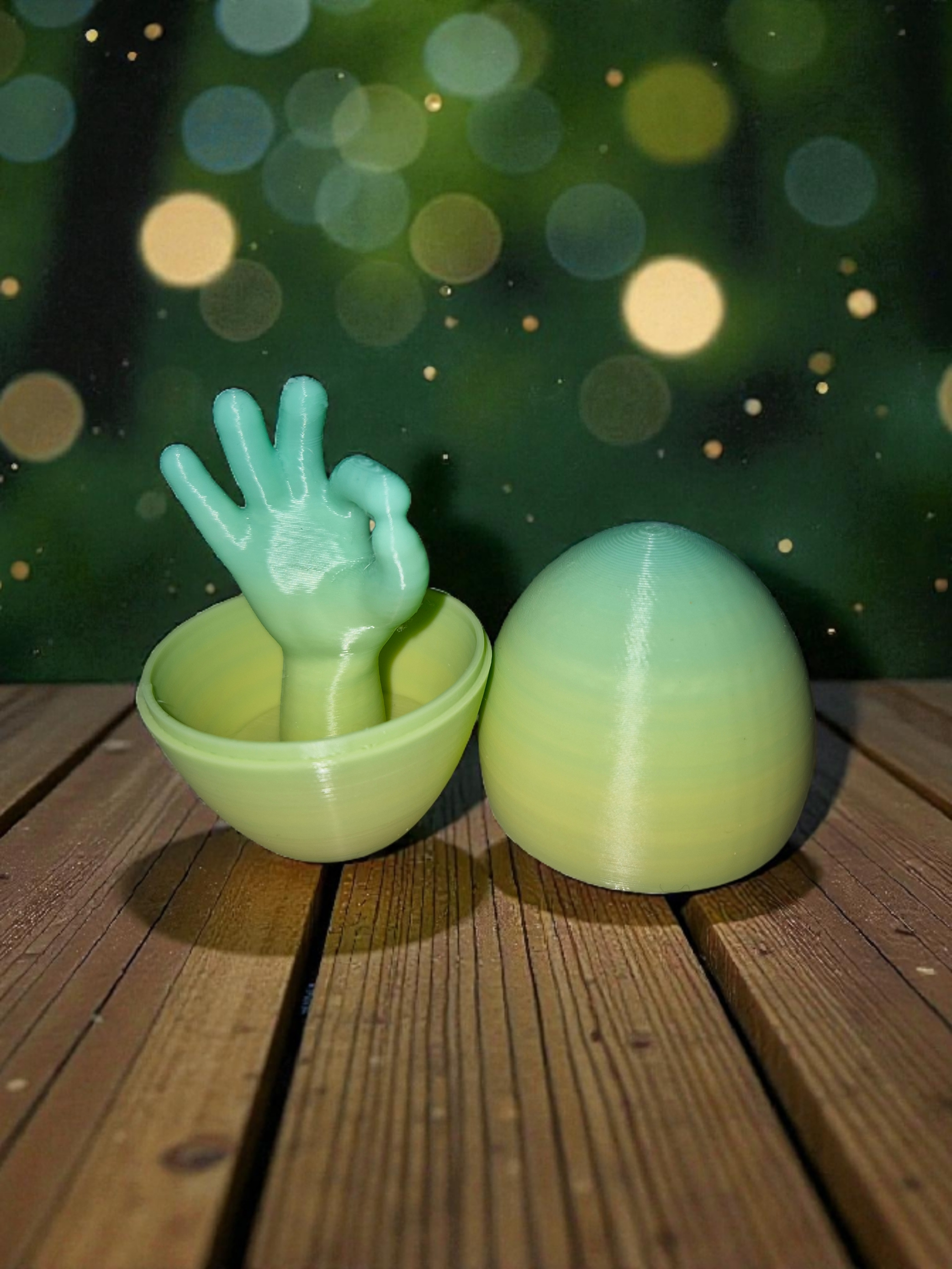 Ein silbernes Ei, das halb aufgeschlagen ist, mit einer grünen, 3D-gedruckten Hand, die eine OK-Geste zeigt, in einem grünen Ei-Schale. Im Hintergrund ist ein dunkler Himmel mit gelblich-weißen Bokeh-Lichtern.