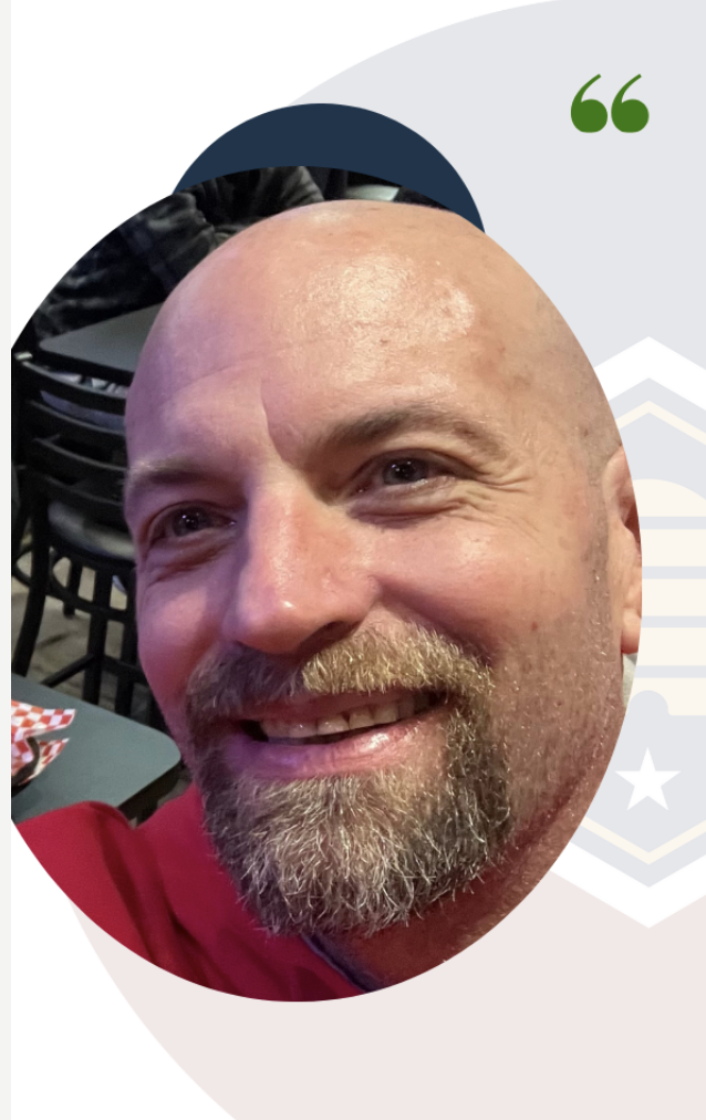 Close-up of a smiling, bald man with a beard, wearing a red shirt, in a casual setting.