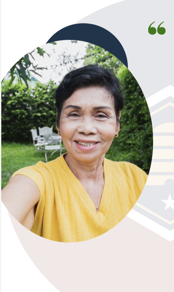 A smiling woman with short black hair taking a selfie outdoors in a green garden, wearing a yellow top.