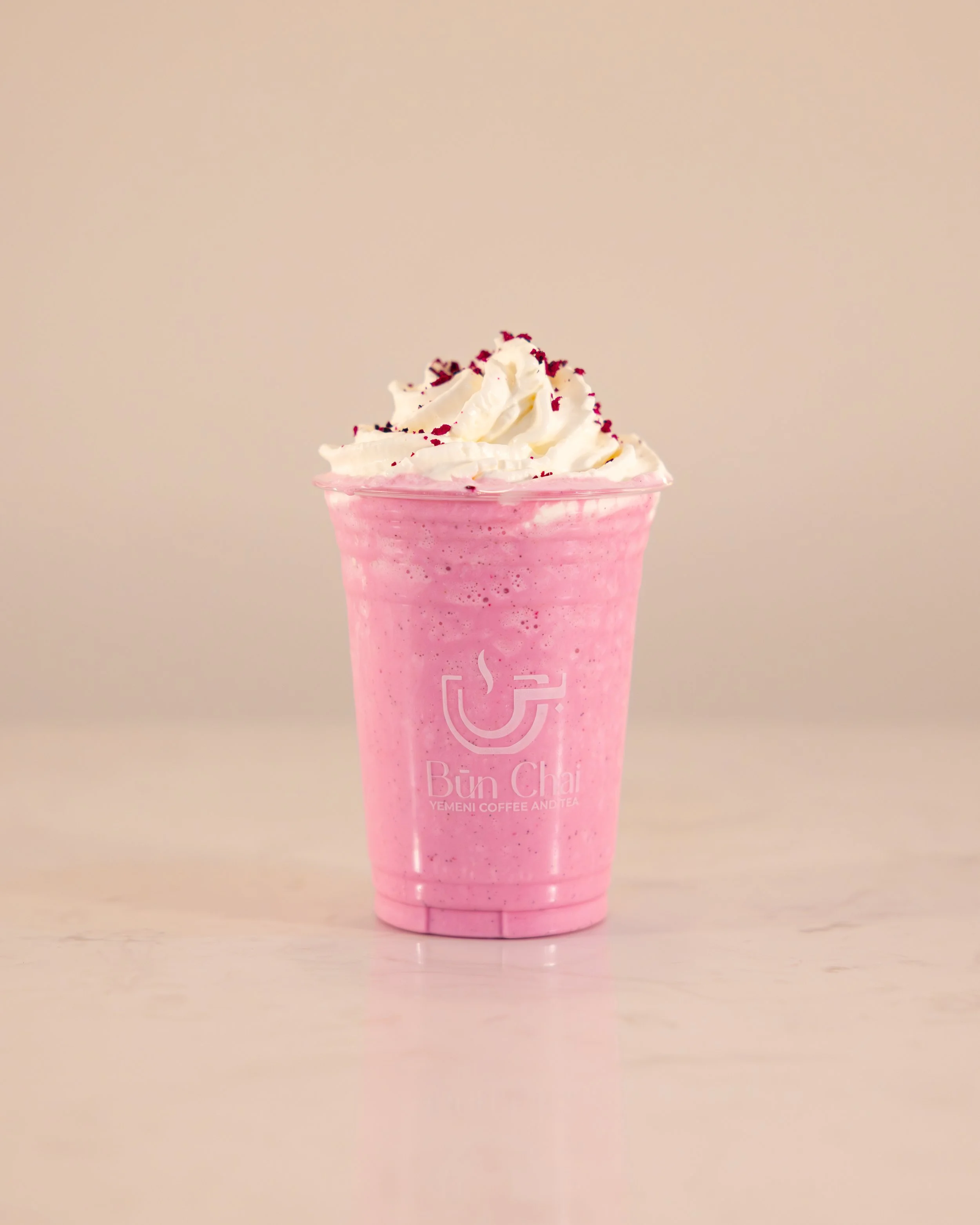 A pink blended beverage in a clear cup topped with whipped cream and red sprinkles, from Bun Chai Yemeni Coffee and Tea.