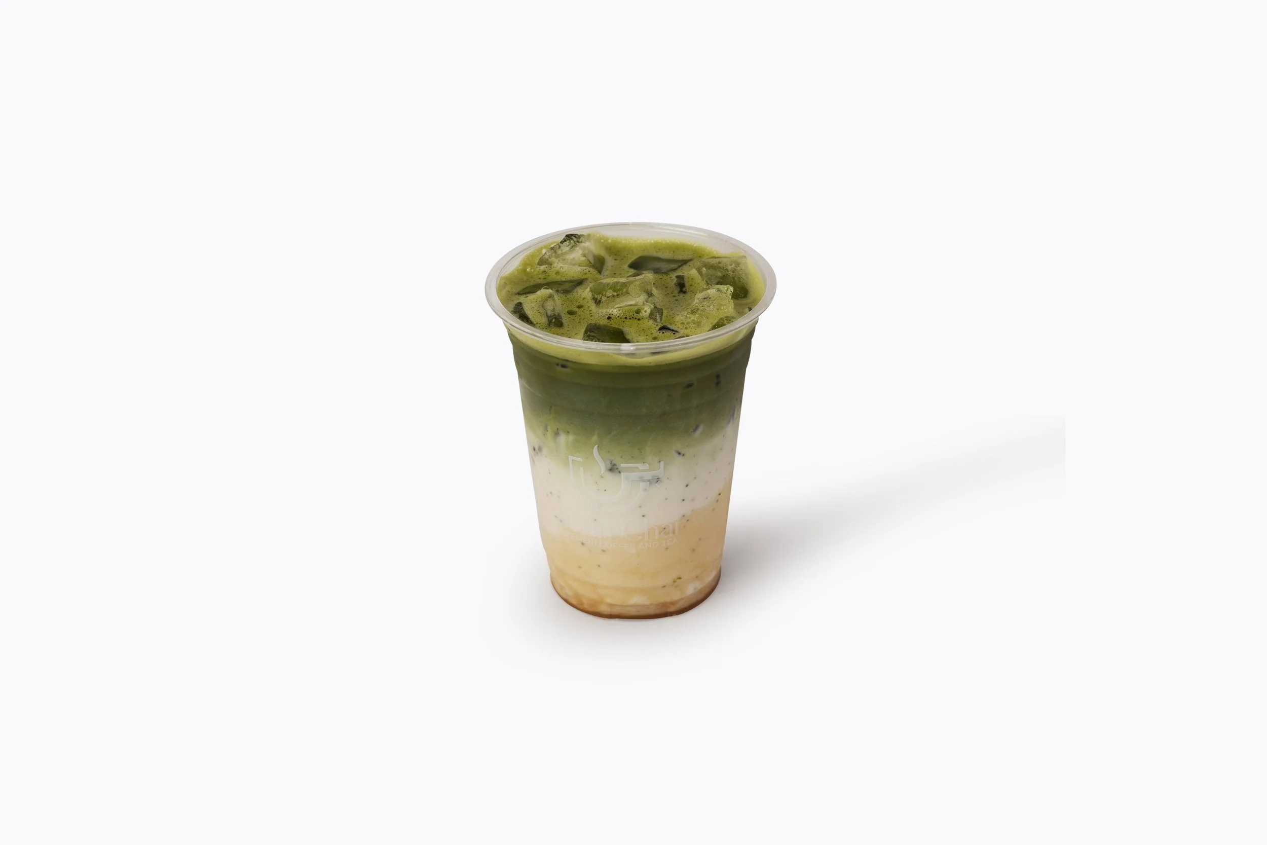 A plastic cup of iced matcha green tea latte with layered green tea, milk, and brown sugar syrup at the bottom, with ice cubes on top.