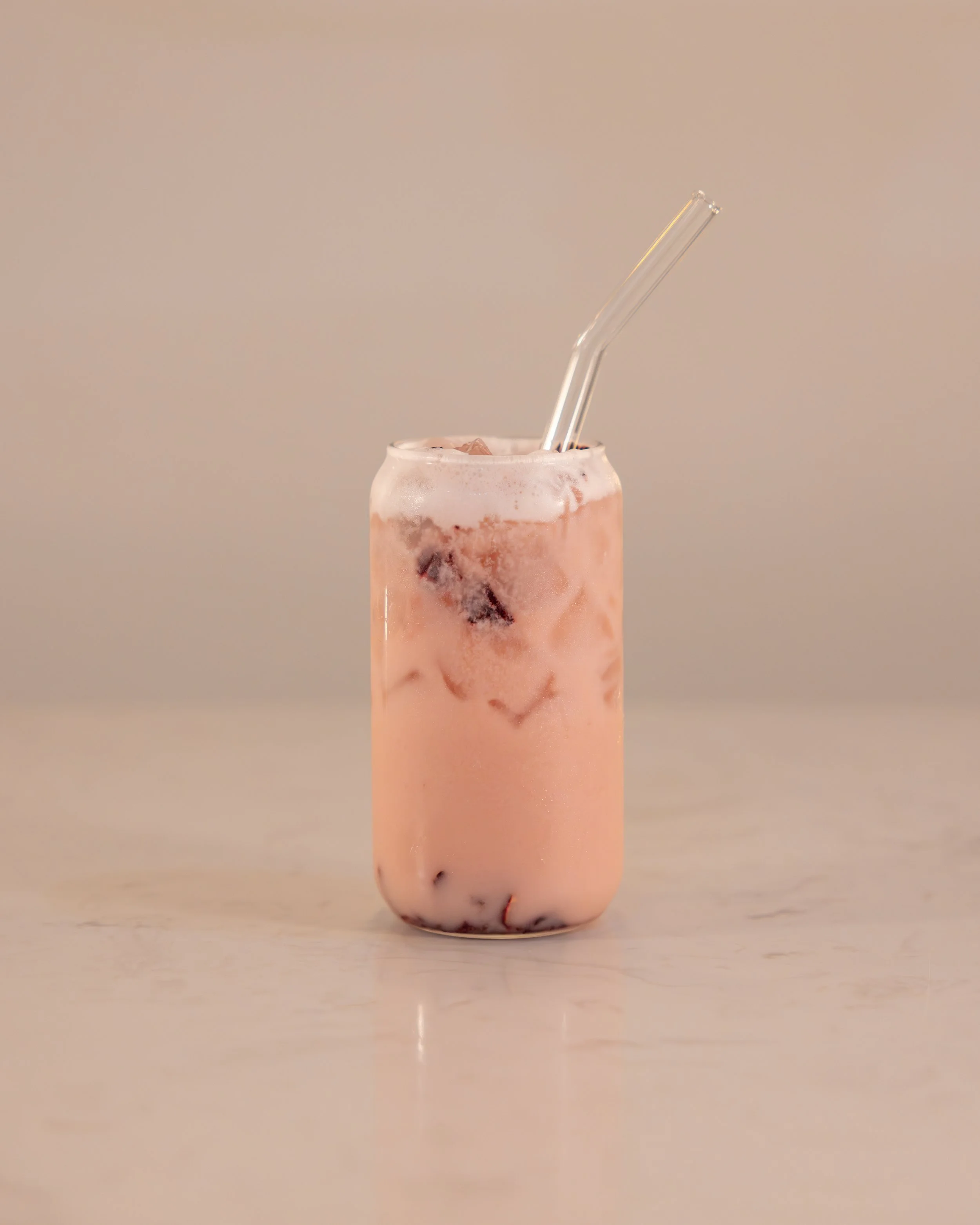 A glass of pink iced beverage with a straw on a light-colored surface.