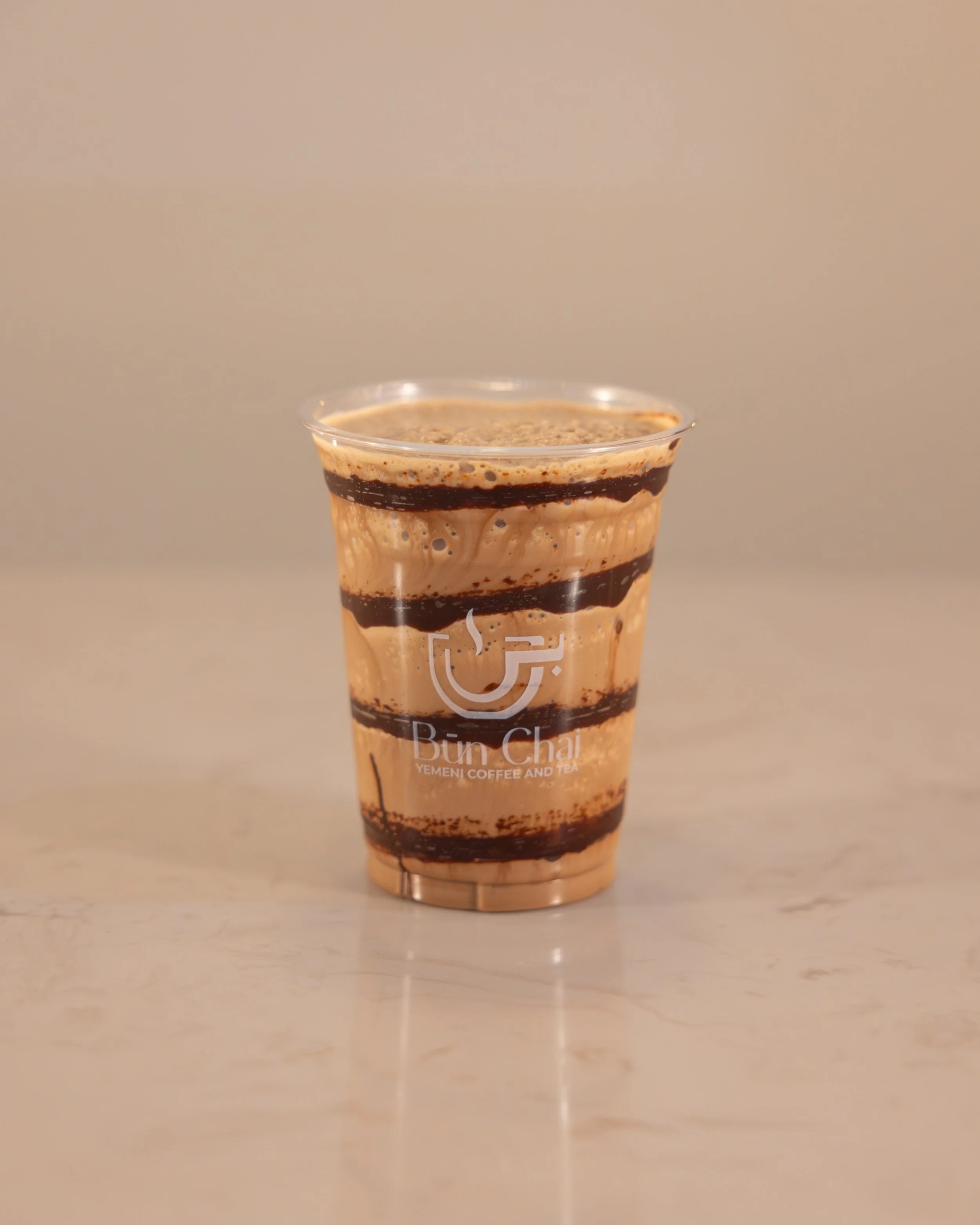 Chocolate frappuccino with whipped cream, chocolate drizzle, and caramel sauce in a clear plastic cup with Bun Chai logo.