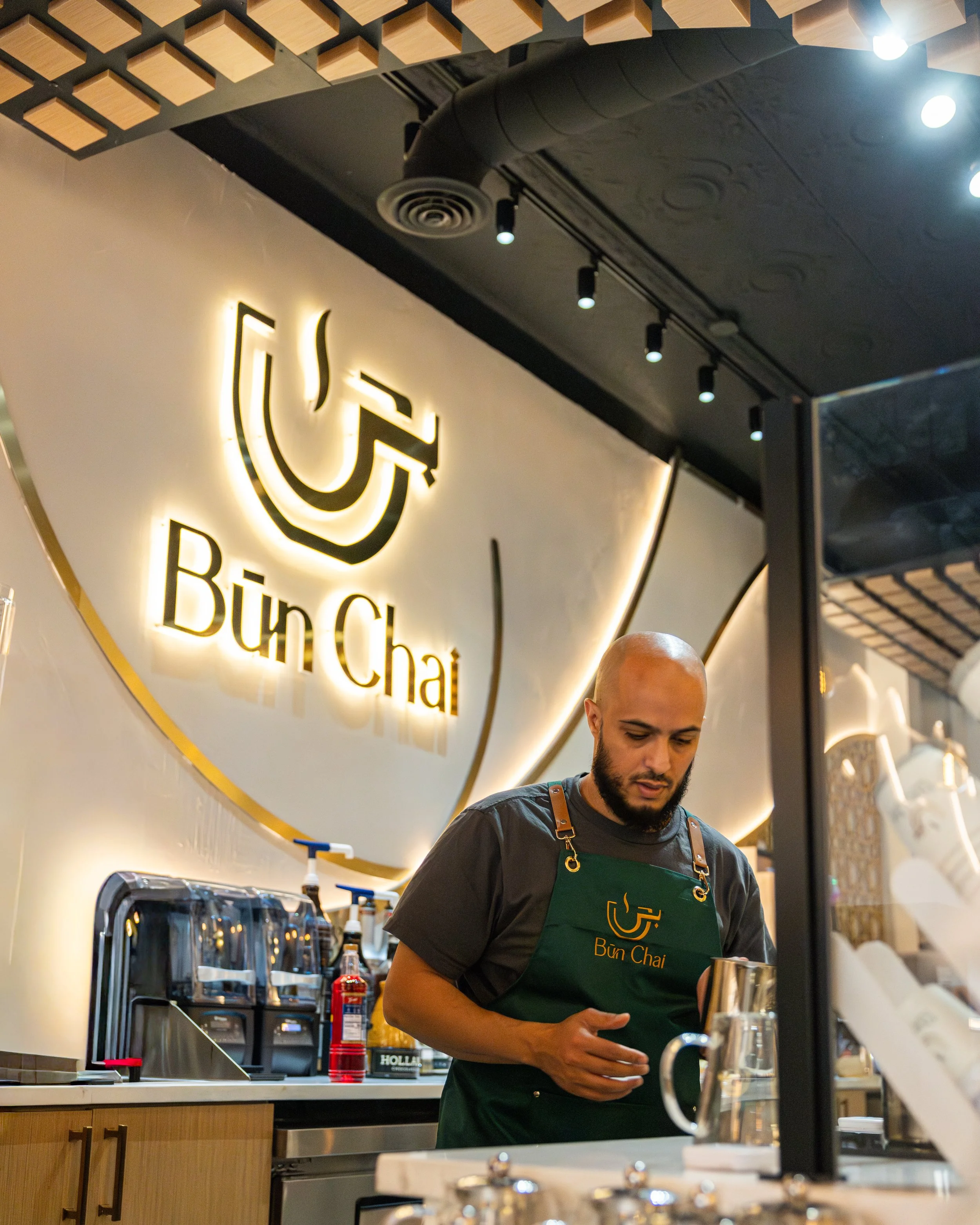 A man working behind the counter at Bun Chai restaurant, with the restaurant's illuminated sign on the wall behind him.