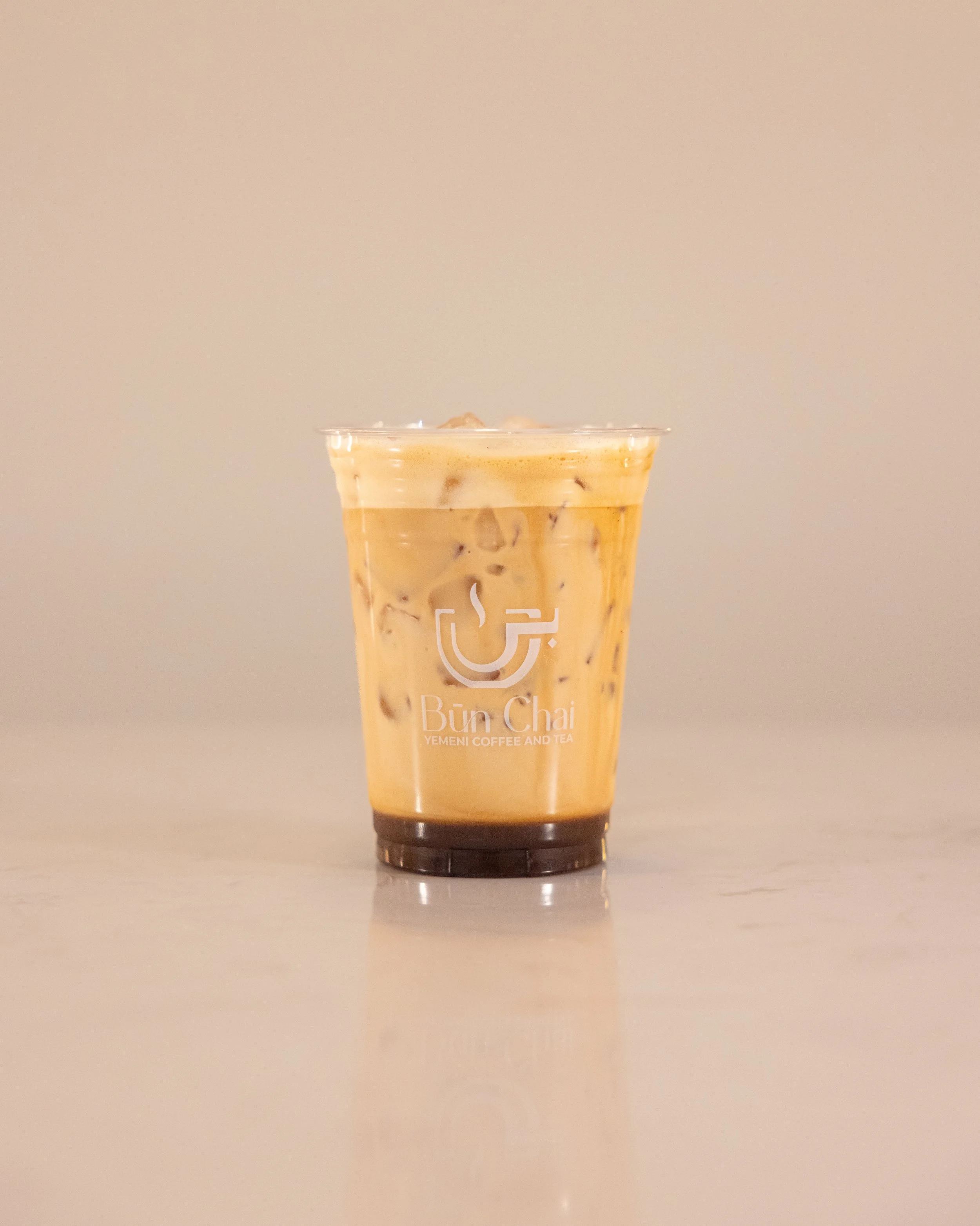 Iced coffee in a plastic cup with a logo and text, on a light-colored surface.