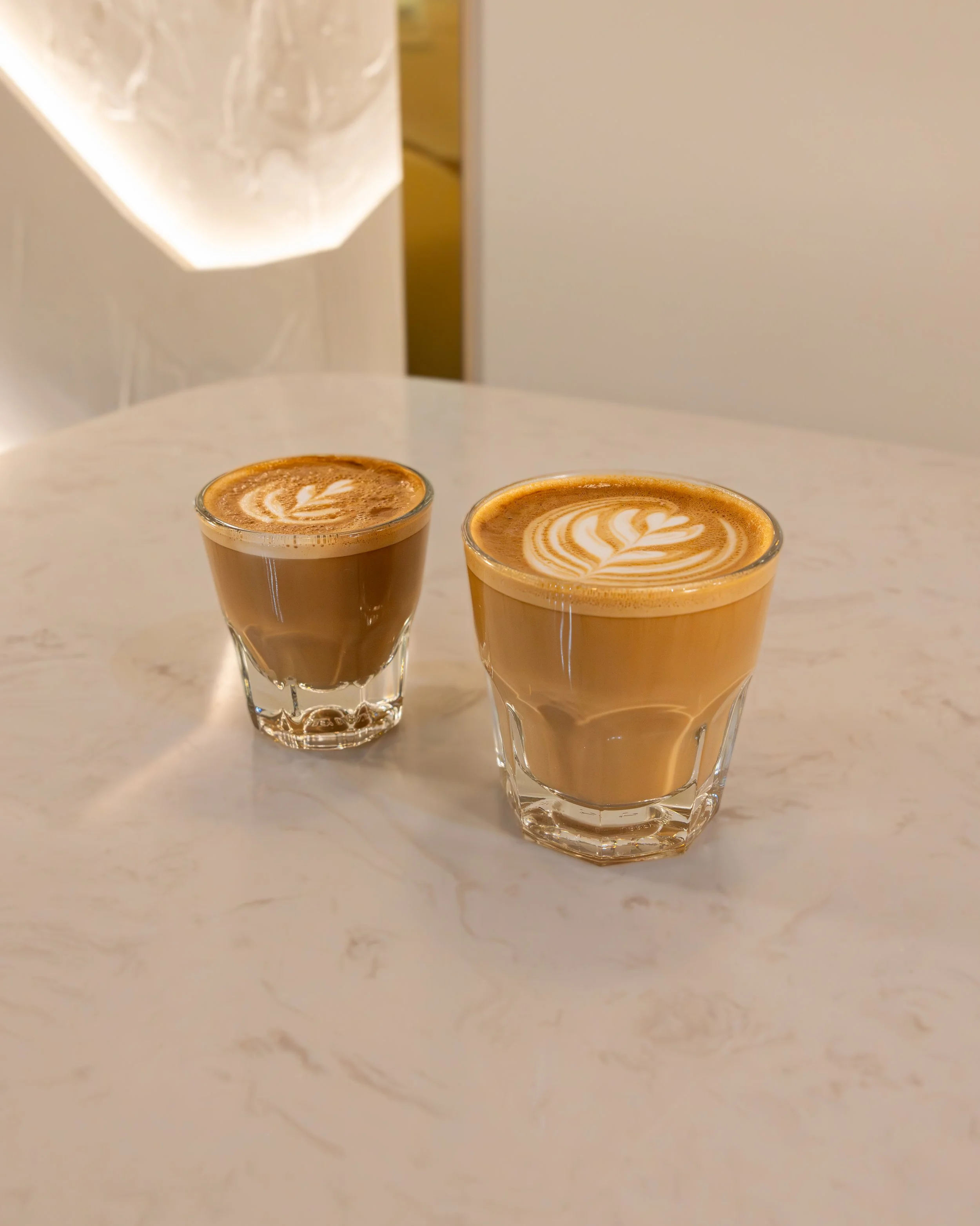 Two glasses of latte with foam art on a marble table.