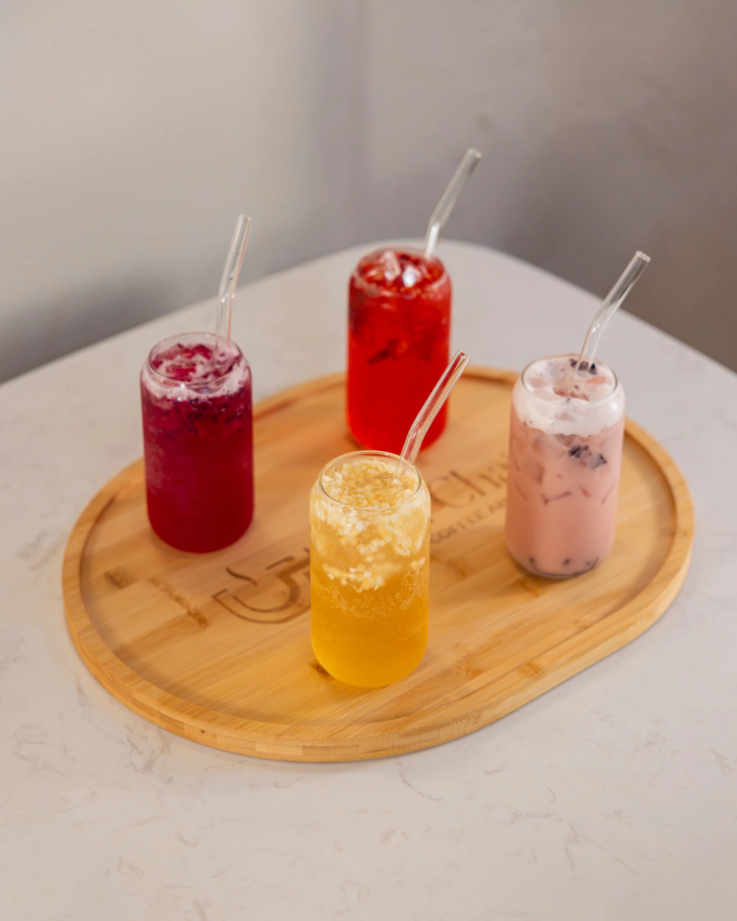 Four colorful drinks in jars with straws on a round wooden tray.