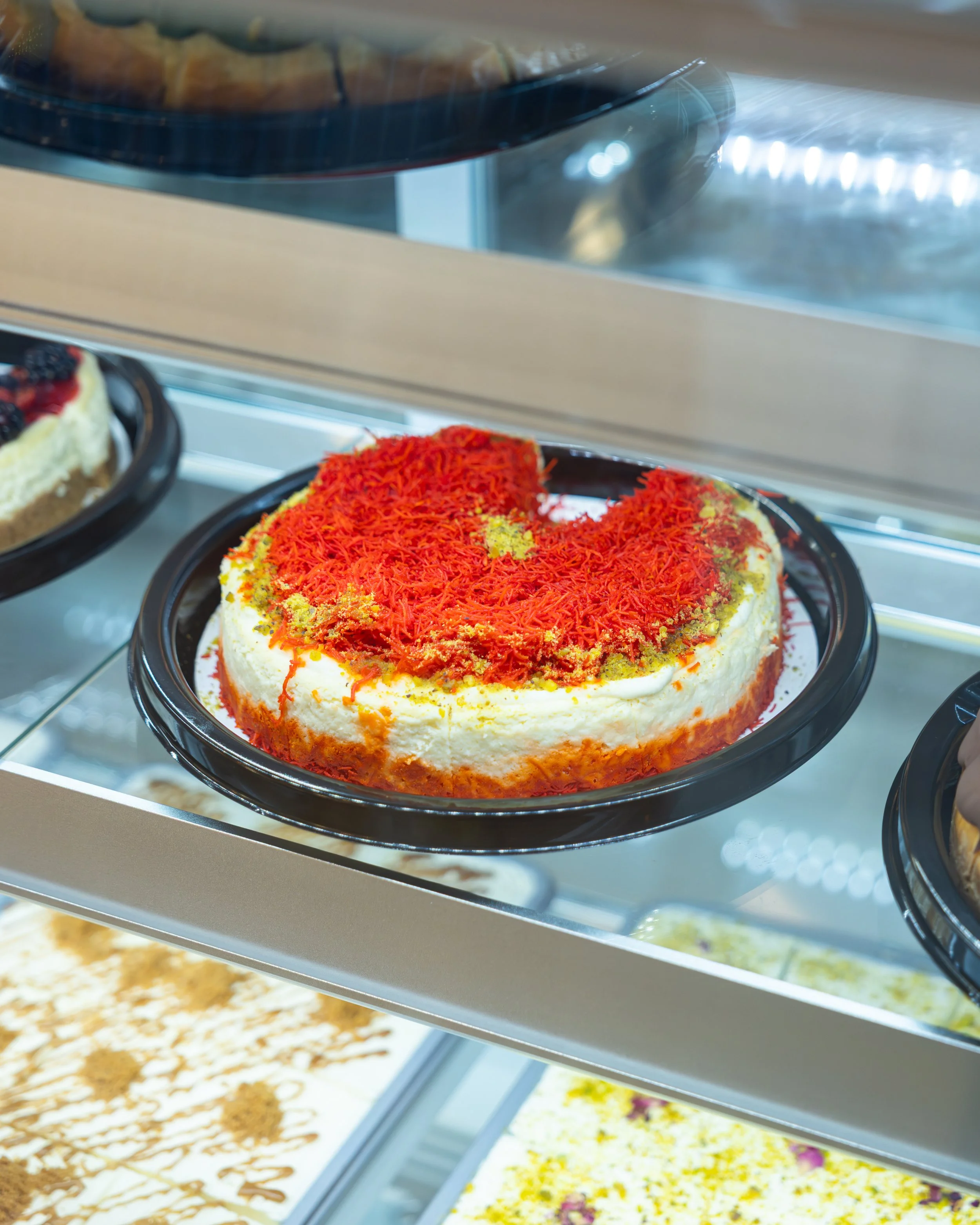Cheesecake decorated with red shreds on top, displayed in a bakery case.