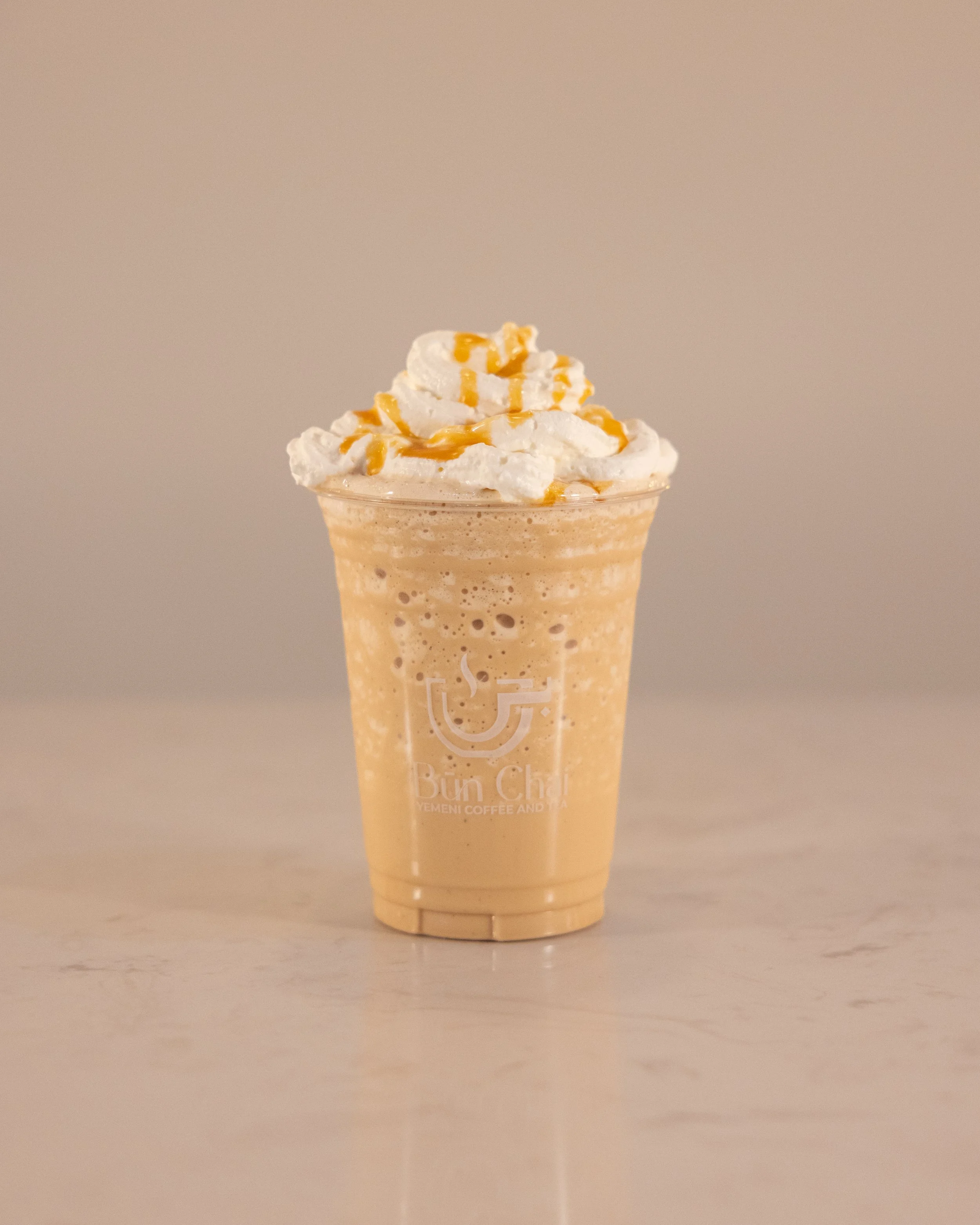 Caramel frappuccino with whipped cream and caramel drizzle in a plastic cup.