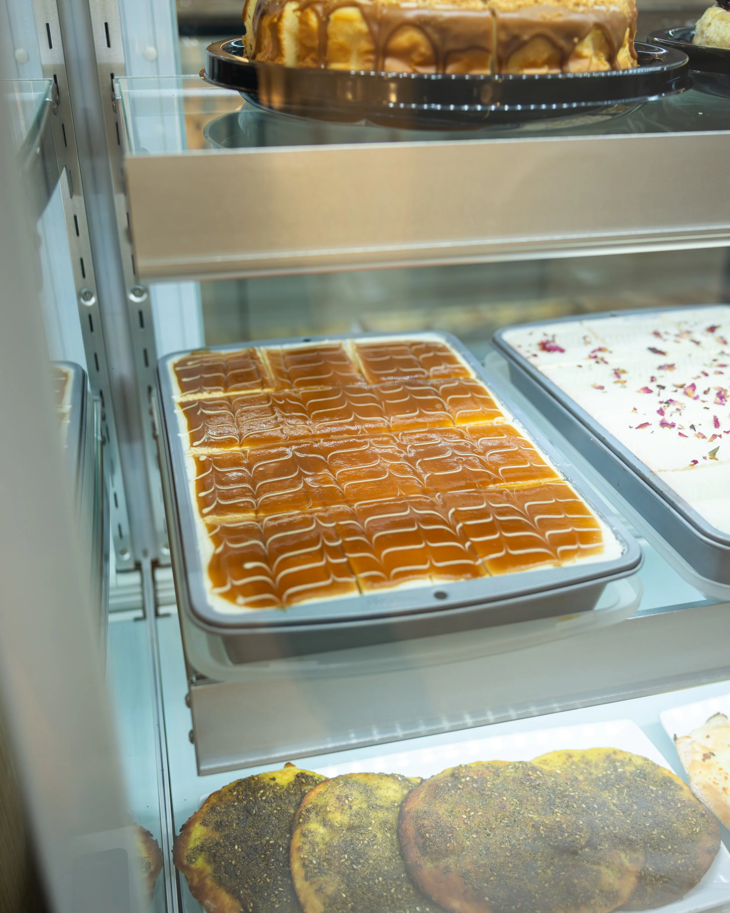 Display case with caramel flan, pastries topped with herbs, and other desserts.