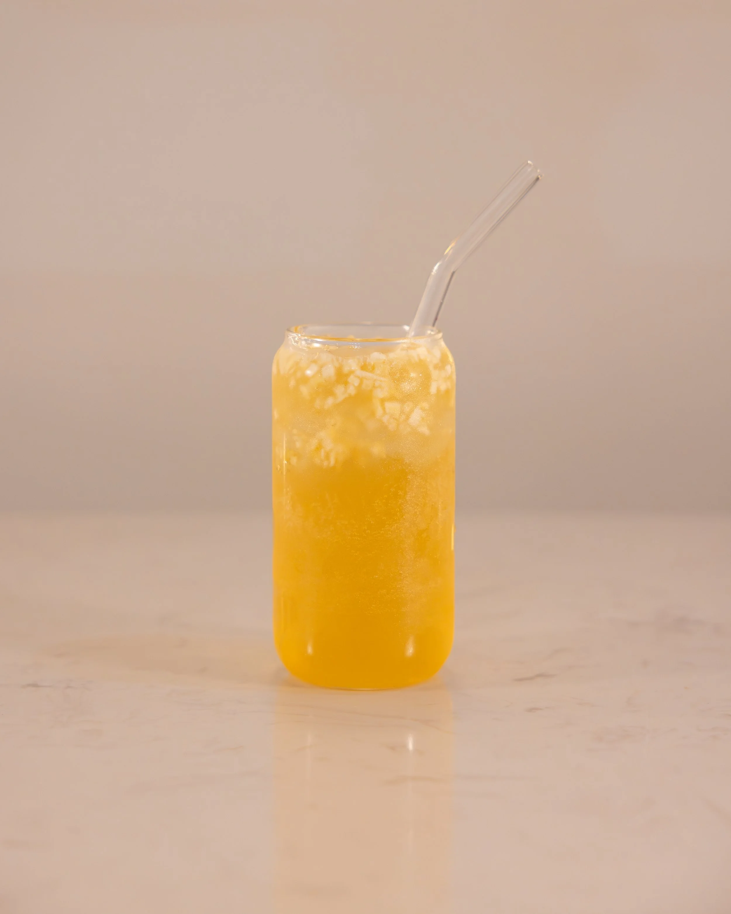 A glass jar filled with a yellow-orange beverage with ice cubes and a strawy.