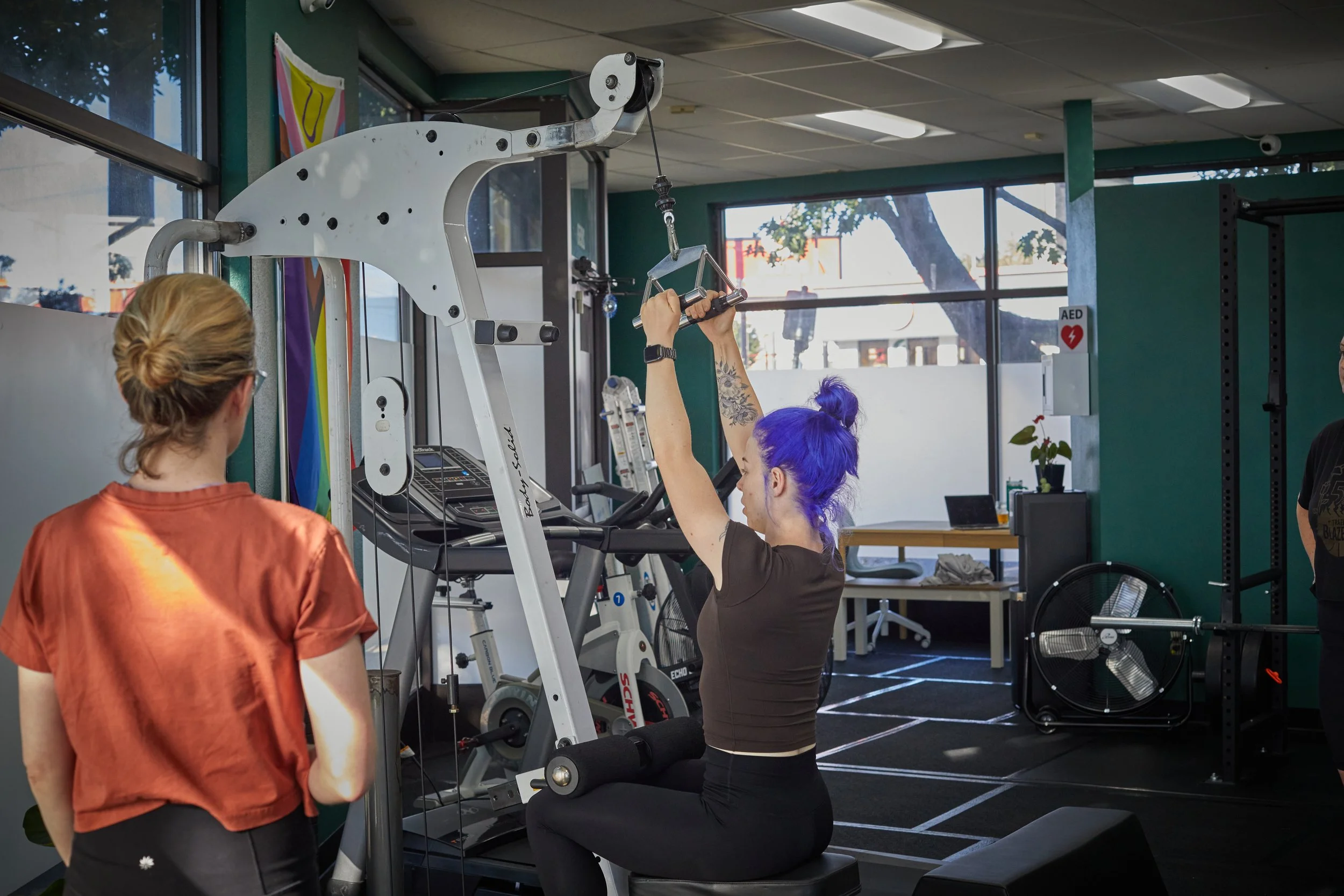 Coach Megan showing a client how to do a cable lat pull down in a gym in Portland, Oregon.