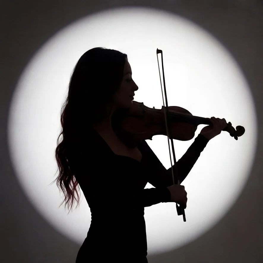 Silhouette of a woman playing the violin, illuminated by a bright circular light in the background.