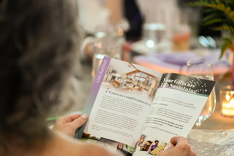 Person holding a brochure at a dining table with wine glasses and candles.