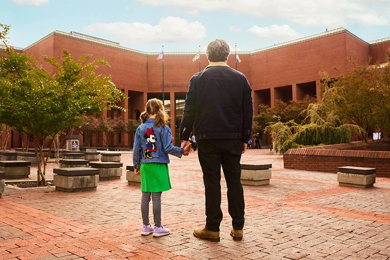 A man and a girl holding hands, standing on the brick-paved courtyard outside the Frederick County Courthouse