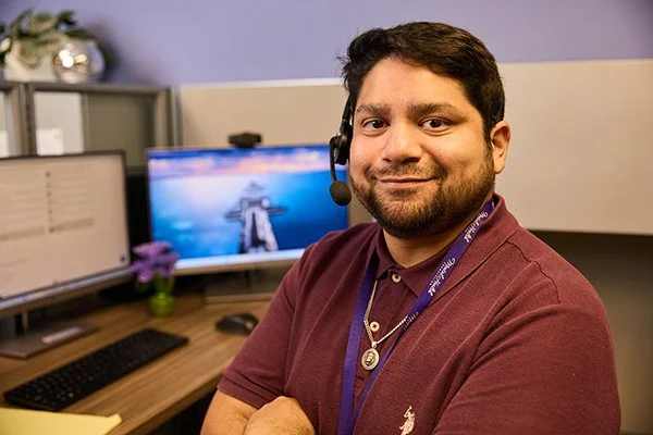 smiling man with headset and MHA badge sit in front of a computer desk