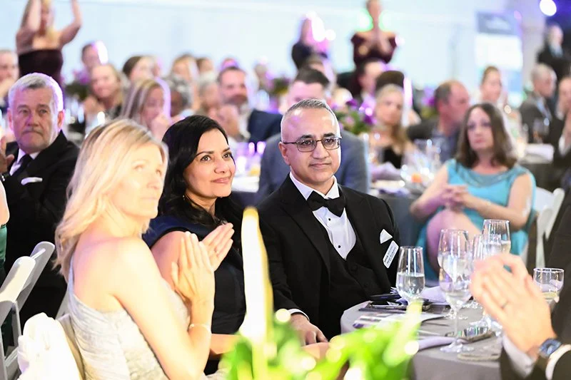 People seated at  the Catoctin Affair, with some clapping and others watching attentively, in a decorated venue with tables, glasses, and floral centerpieces.