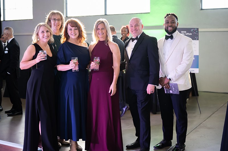 Six people dressed in formal attire at the Catoctin Affair, holding drinks and smiling for the camera inside a well-lit room.