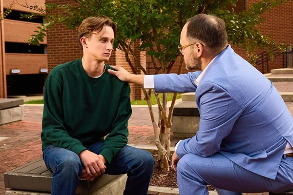 Man in suit jacket supportively puts hand on teenagers shoulder