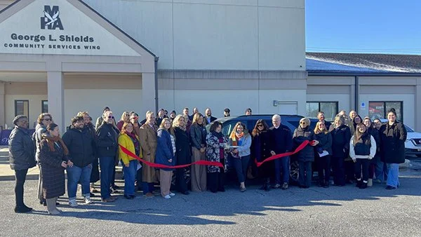 group of people stand with big ribbon in front of MHA offices for grand opening ceremony
