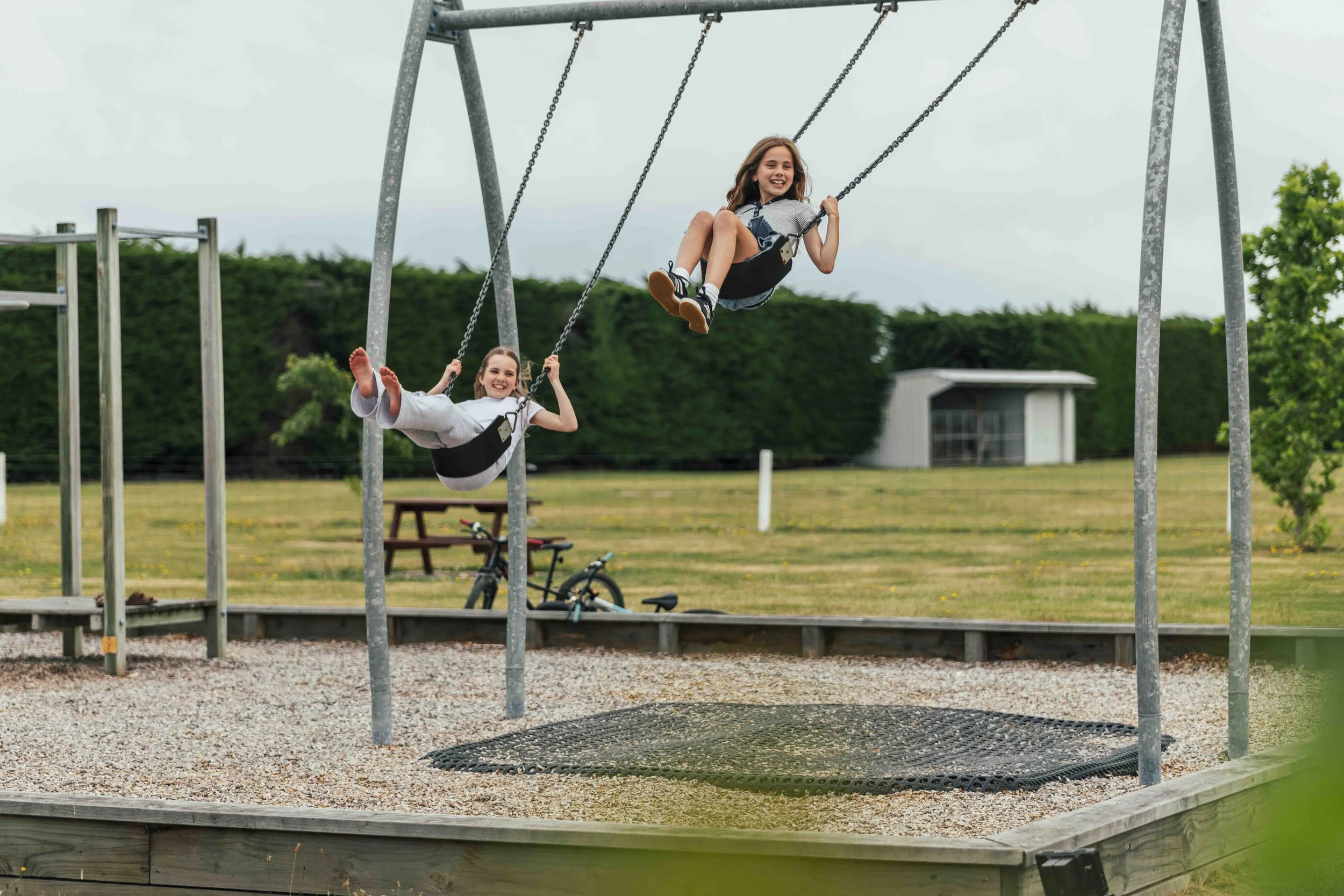 Two young girls smiling and swinging on a playground swing set outdoors.