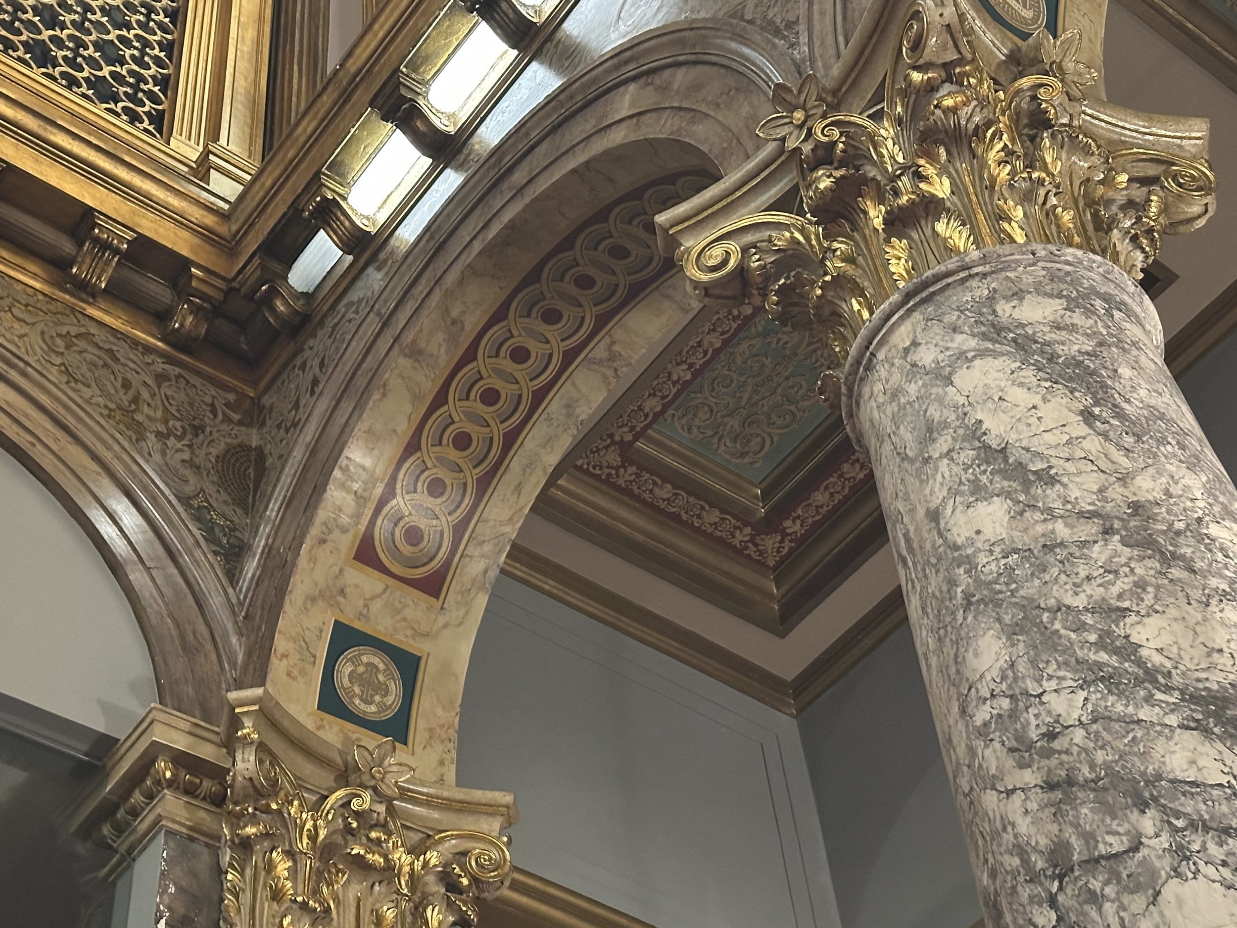 Ornate classical architecture with marble columns and gilded decorative moldings in a building interior.