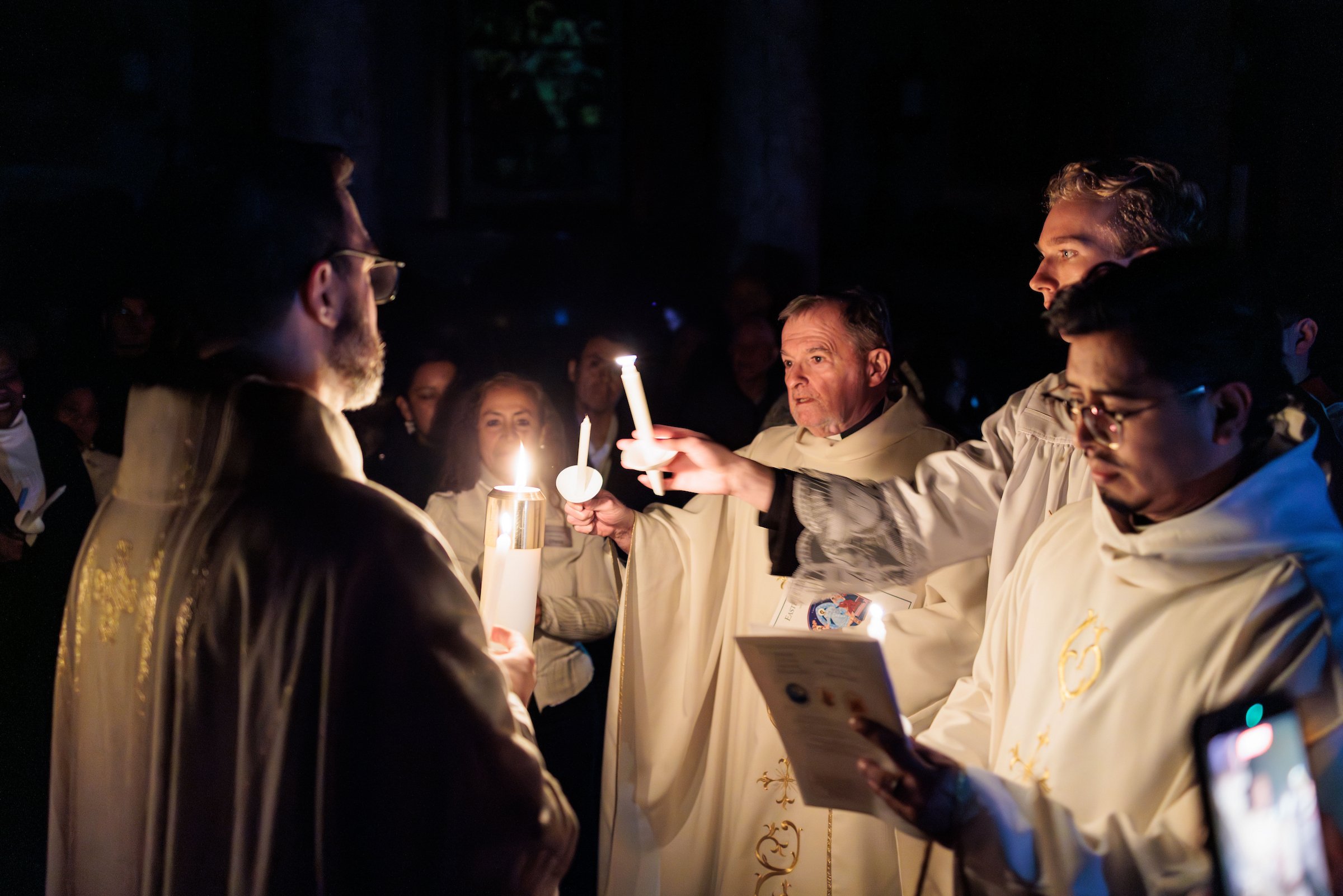 A religious ceremony with priests and congregation holding candles in a dark church.