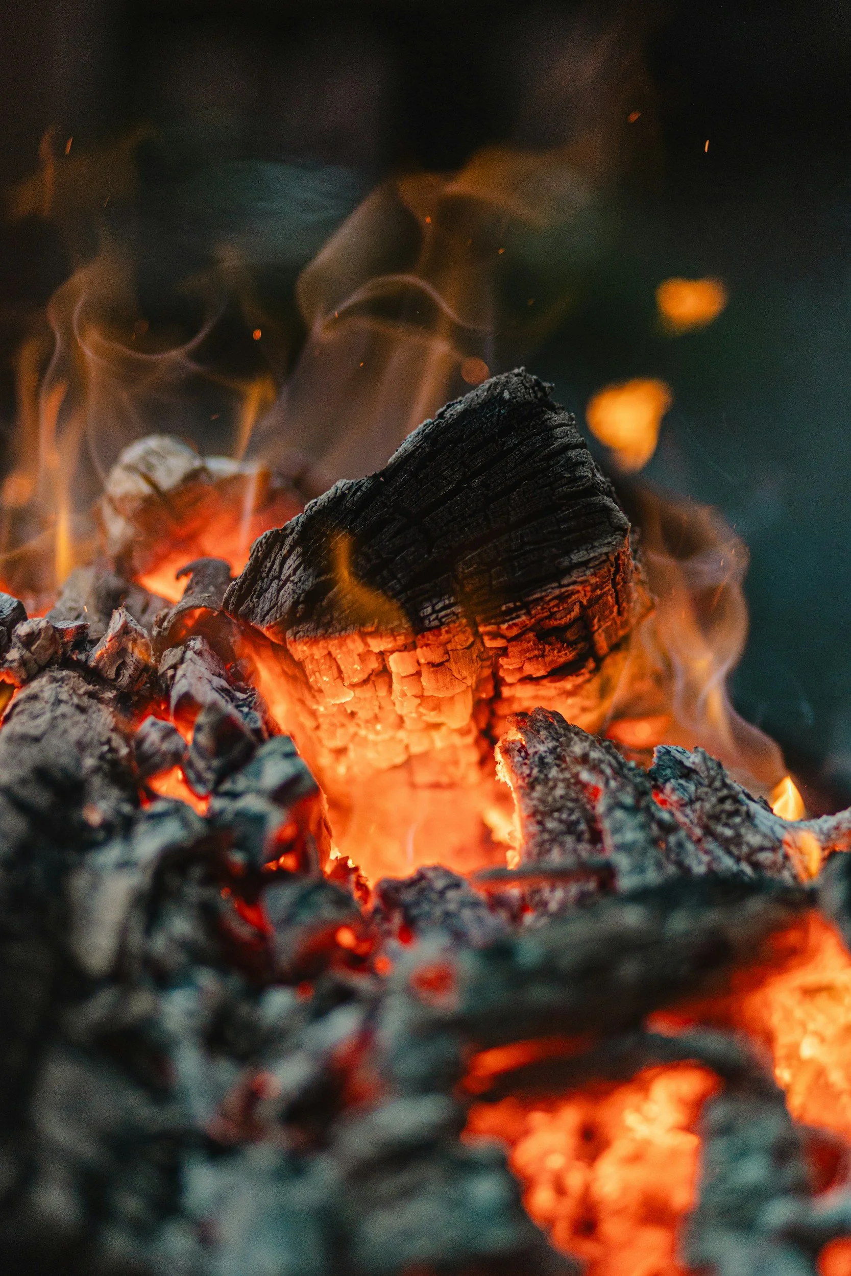 A close-up of burning wood with glowing embers and flames.
